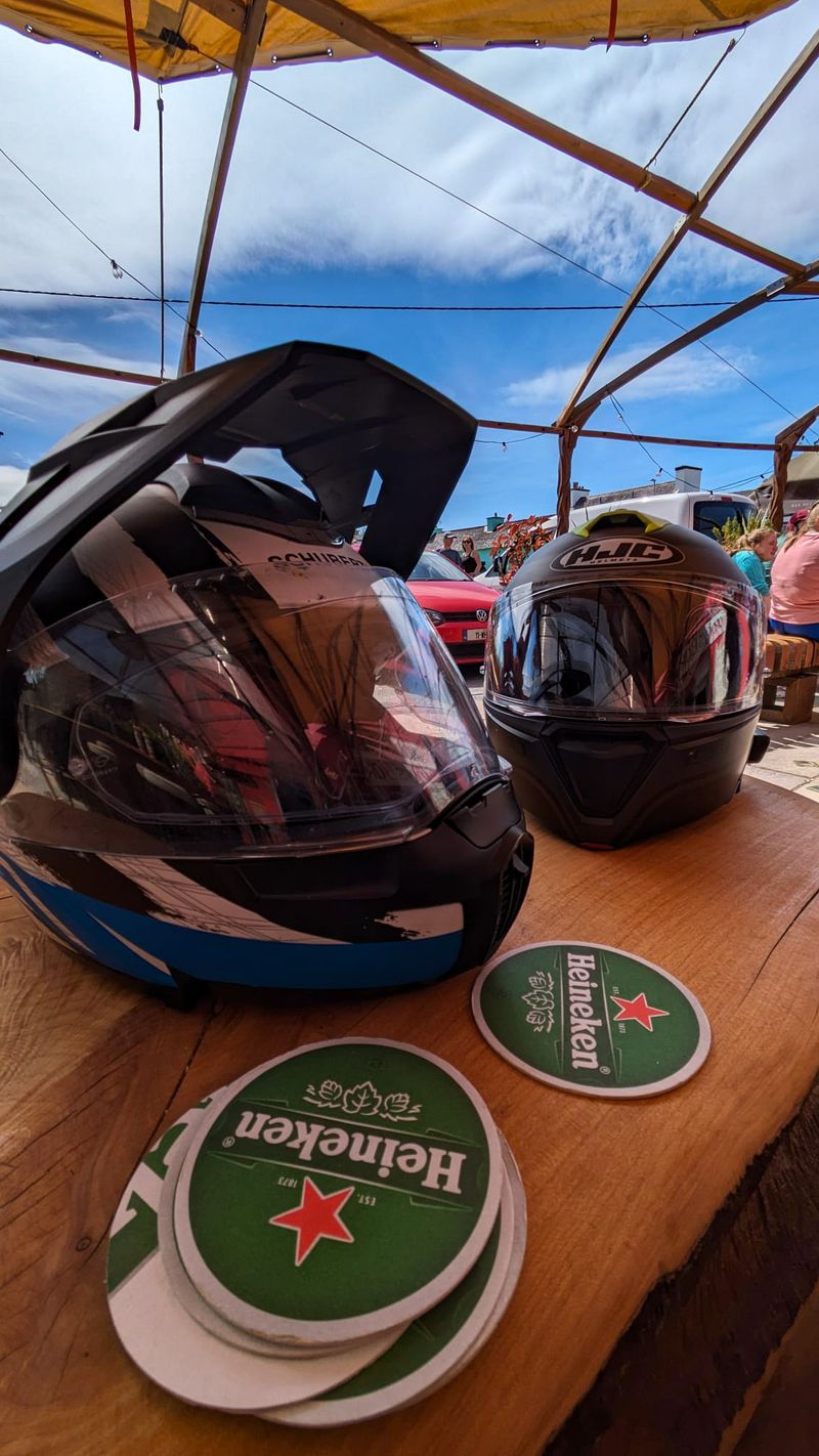 Two motorcycle helmets resting on a pub garden table beside beer mats during a tour stop in Ireland
