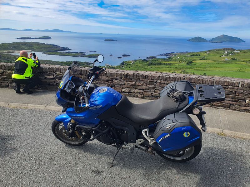Blue Triumph Tiger motorcycle parked at the Coomakista viewpoint overlooking Derrynane Bay and islands on the Ring of Kerry
