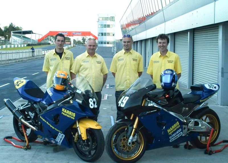 Race team in yellow shirts standing behind two sponsored superbikes in a pit lane in Ireland