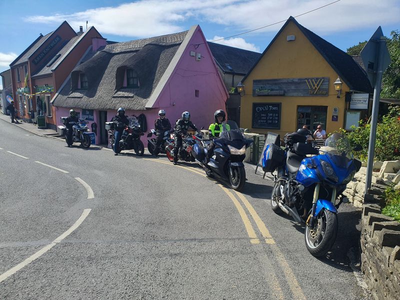 Motorcycles and riders parked outside colourful cottages including a pink thatched shop in Doolin, County Clare