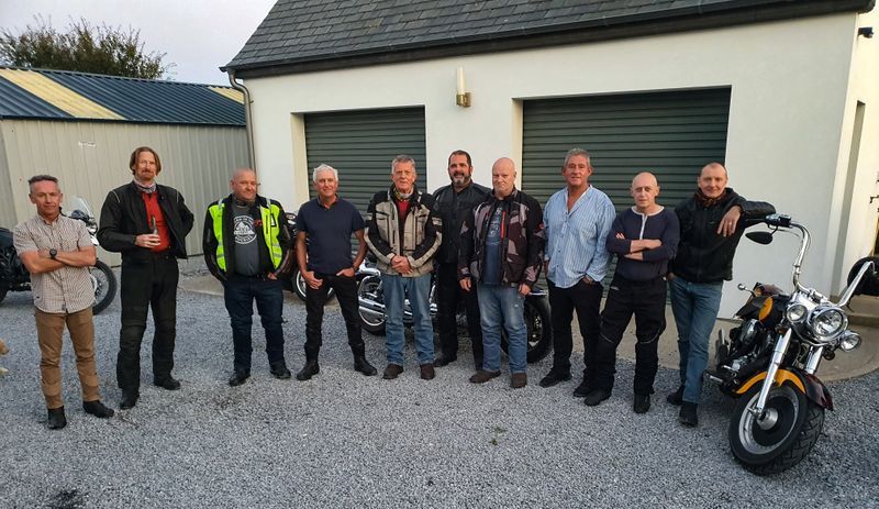 Group of ten motorcyclists posing together in front of a garage at the end of a day's riding