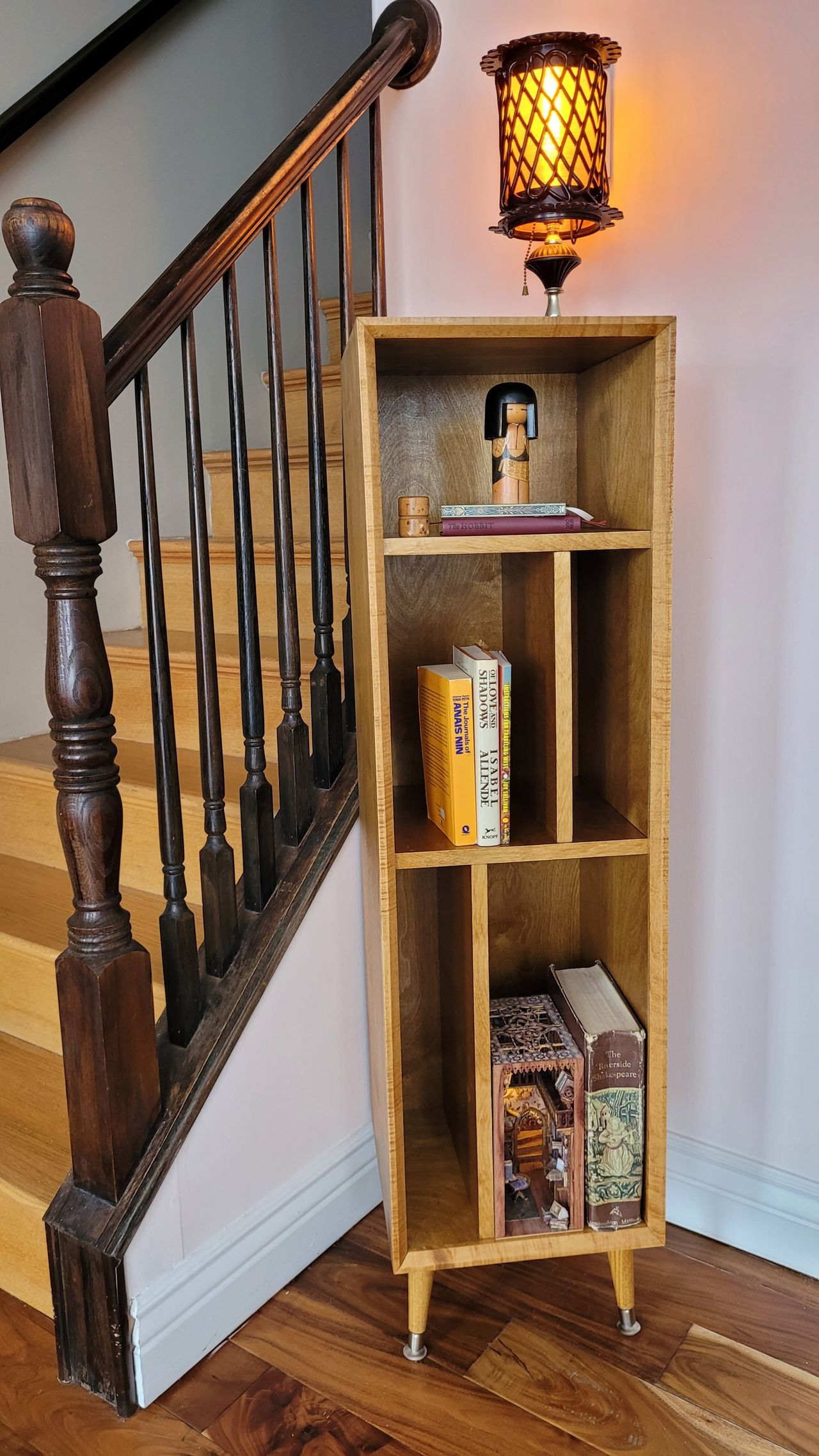 Tall narrow bookcase on tapered legs, filled with books and a lantern on top