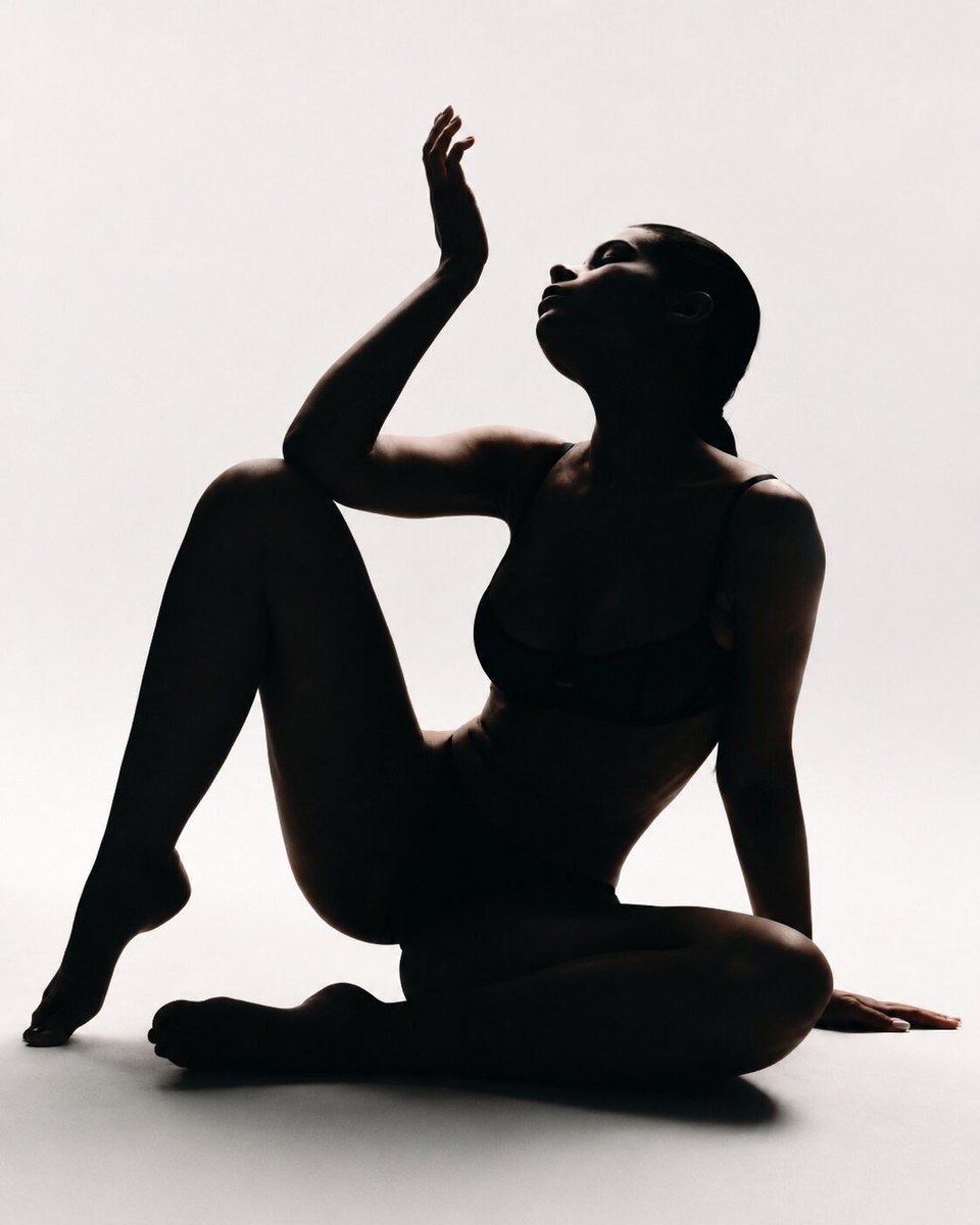 Seated model in silhouette raising one hand against a softly lit white background