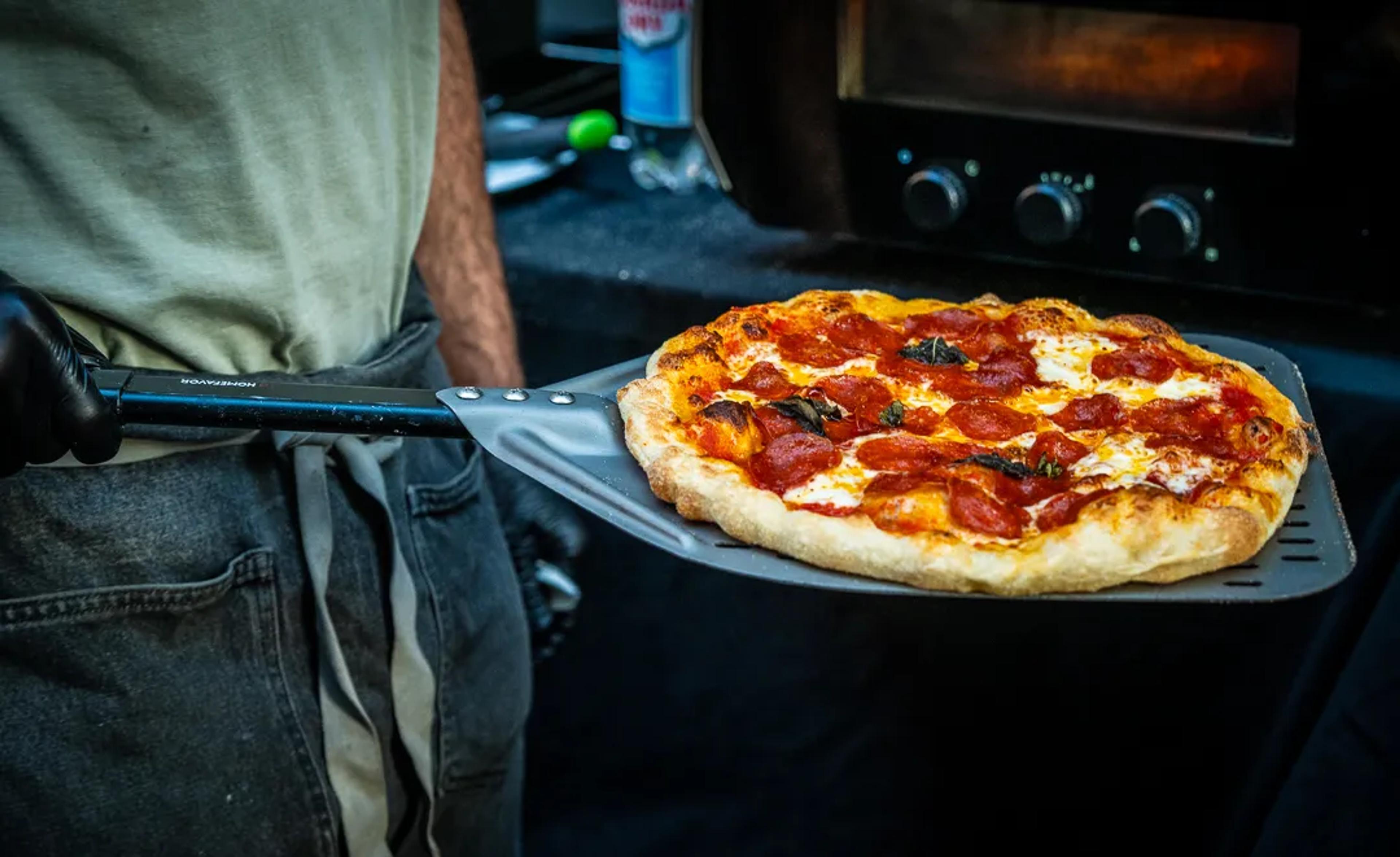 A pepperoni pie coming out of the oven on a peel