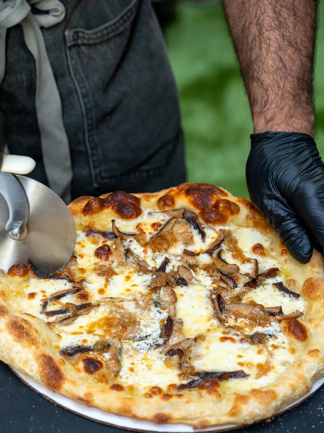 A gloved hand holding a mushroom white pie steady while a wheel cuts it