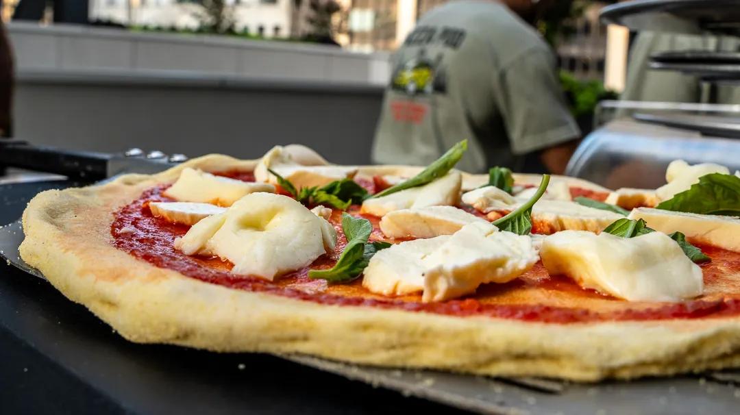 A margherita with torn fresh mozzarella and basil, a cook in a Pizza Pod shirt behind it