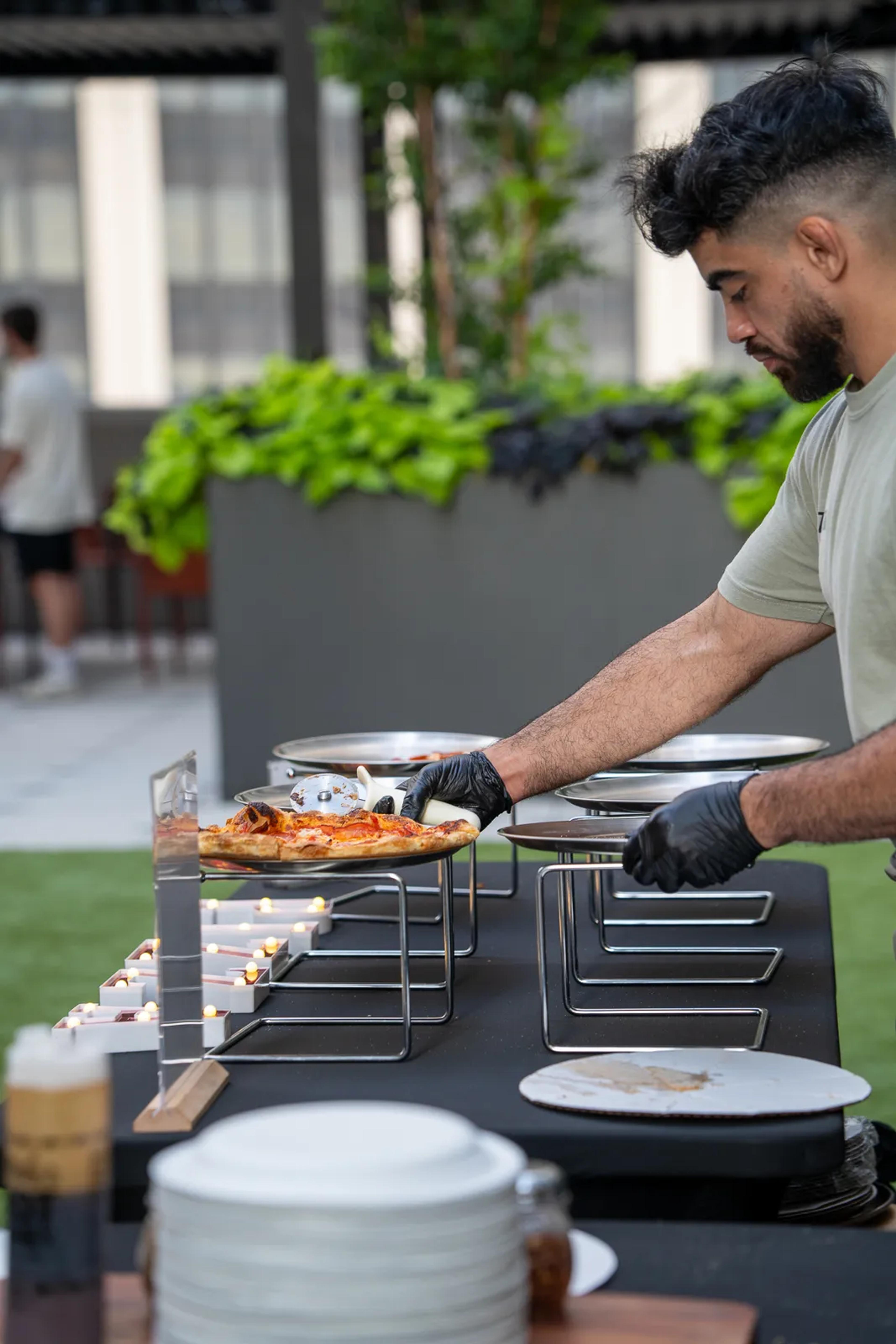 A cook lifting a finished pie onto a raised stand at the service table