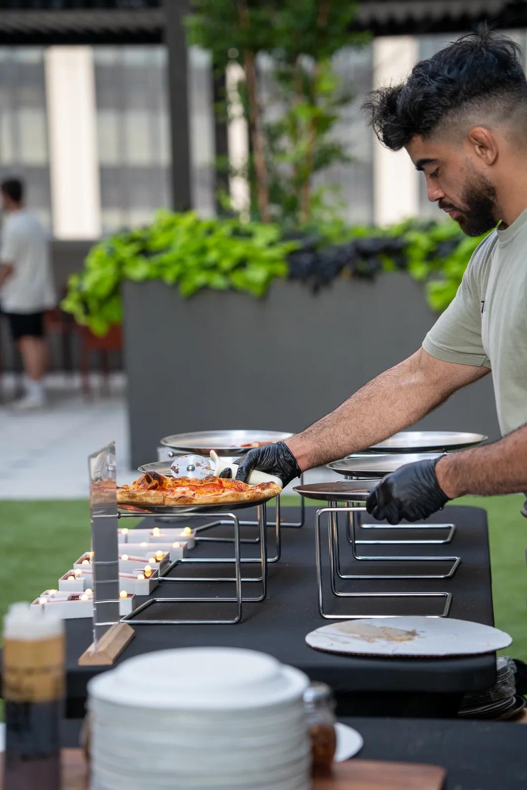 A cook lifting a finished pie onto a raised stand at the service table