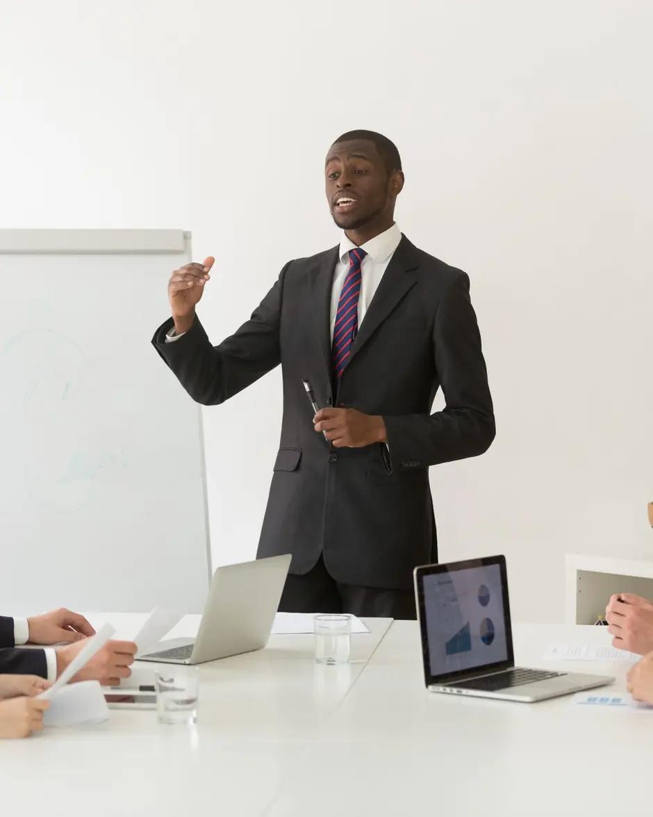 Un consultant présente, debout, devant un tableau blanc, à des collaborateurs attablés.