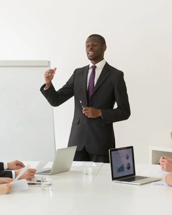 Un consultant présente, debout, devant un tableau blanc, à des collaborateurs attablés.