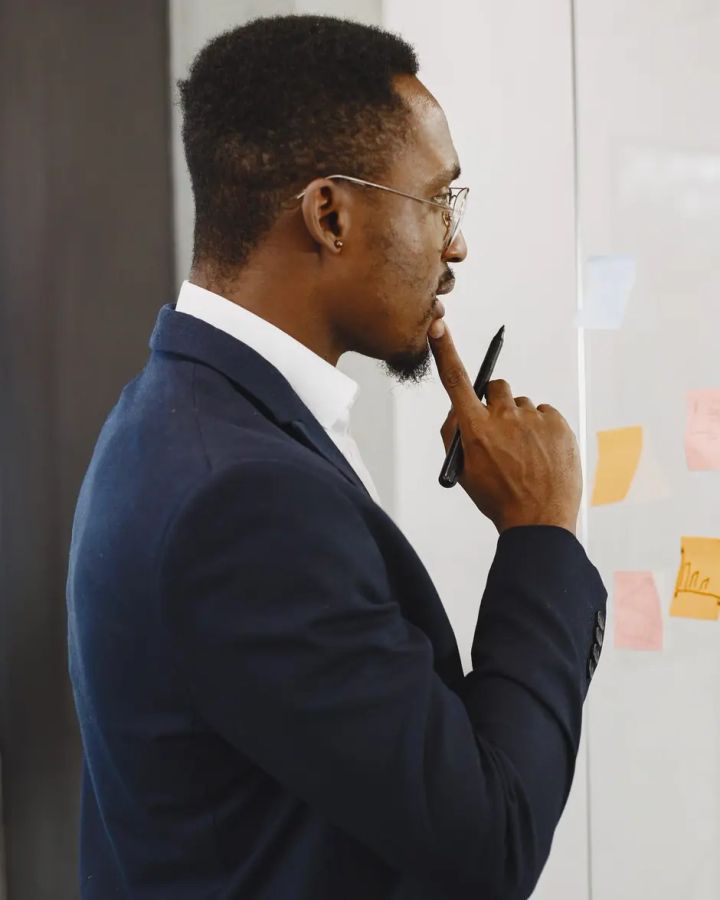 Un cadre réfléchit devant un tableau blanc couvert de notes et de graphiques.