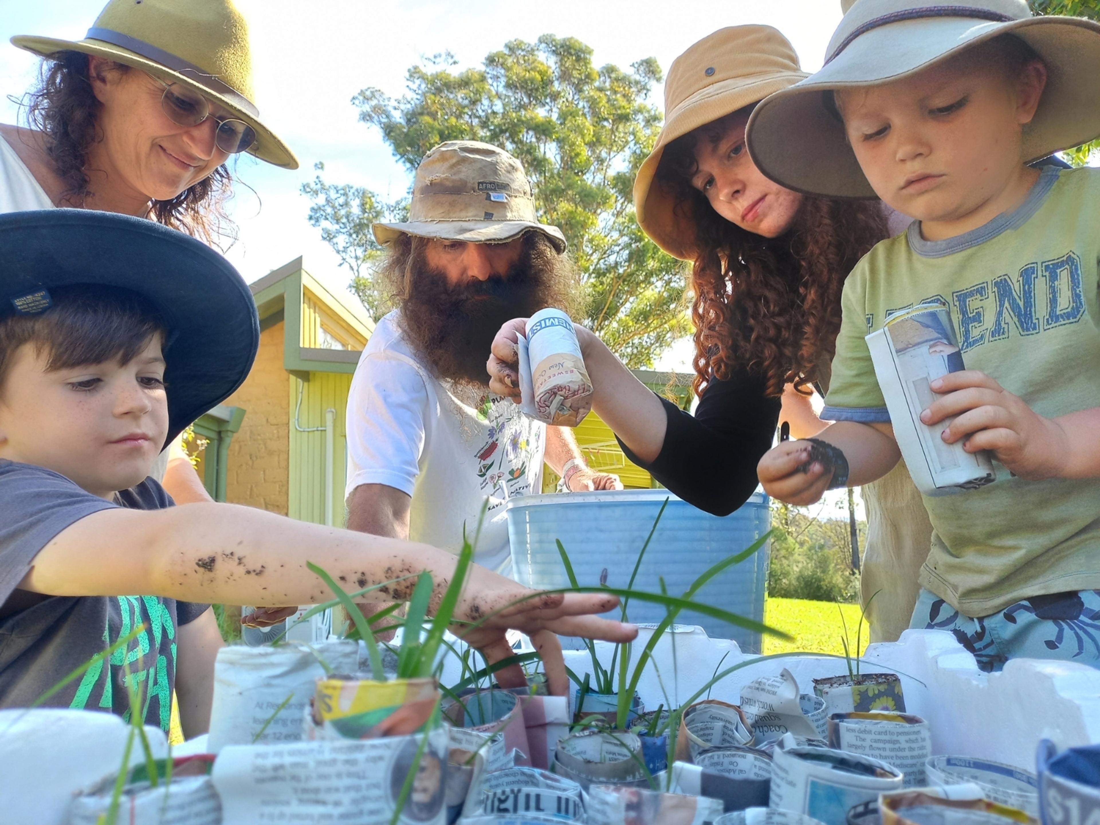3 adults and 2 children planting using small pots made from newspaper.