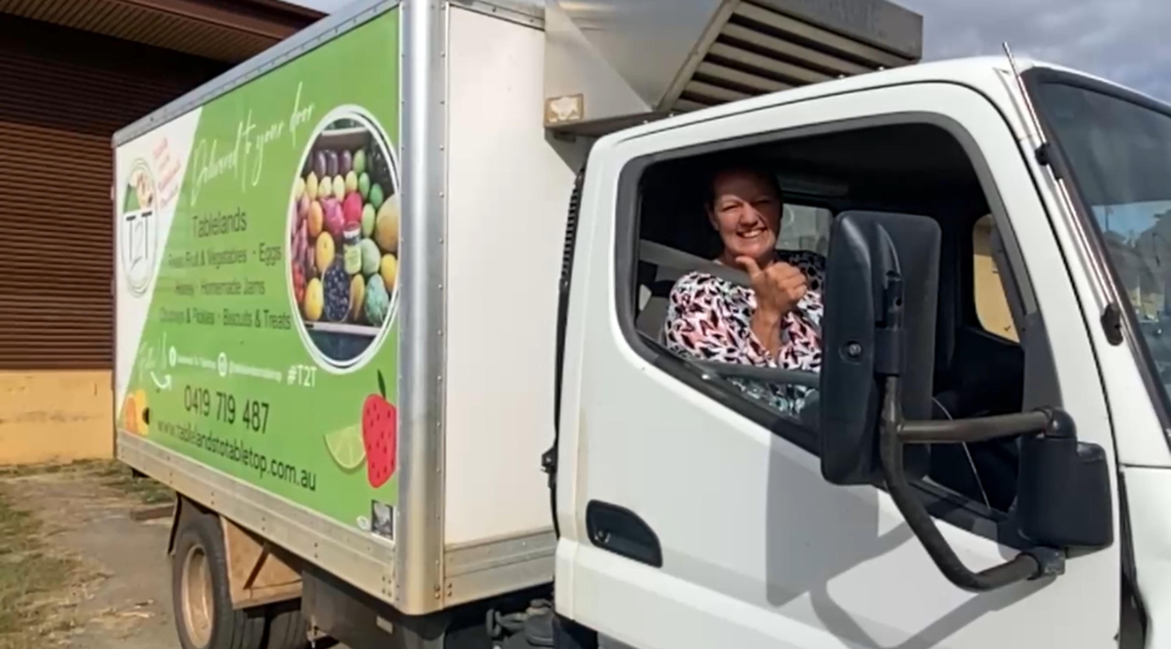 A smiling woman sitting behind the wheel of a small delivery truck. She is giving the camera a big thumbs up.