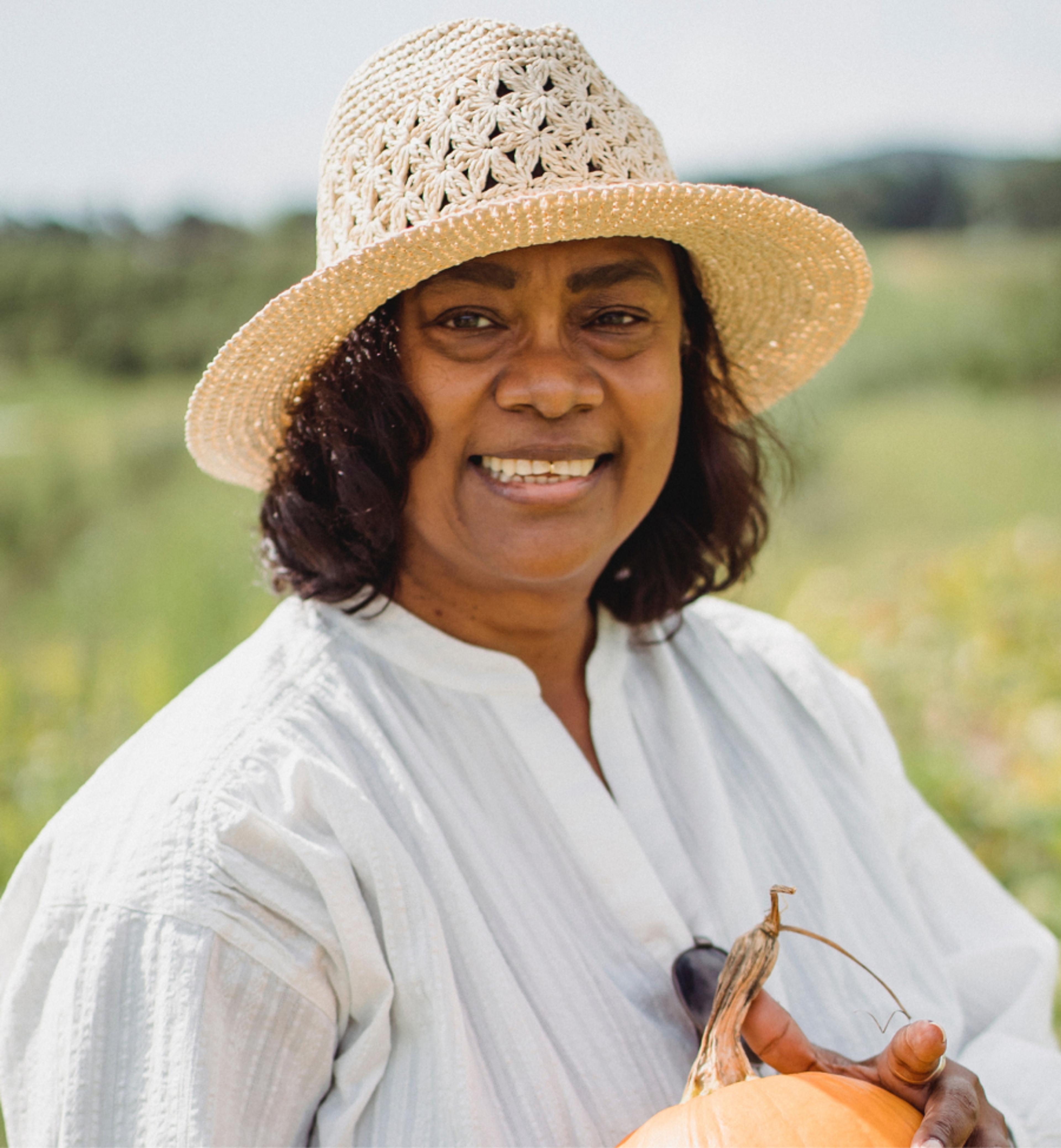 A smiling person with a hat in a field holding a pumpkin.