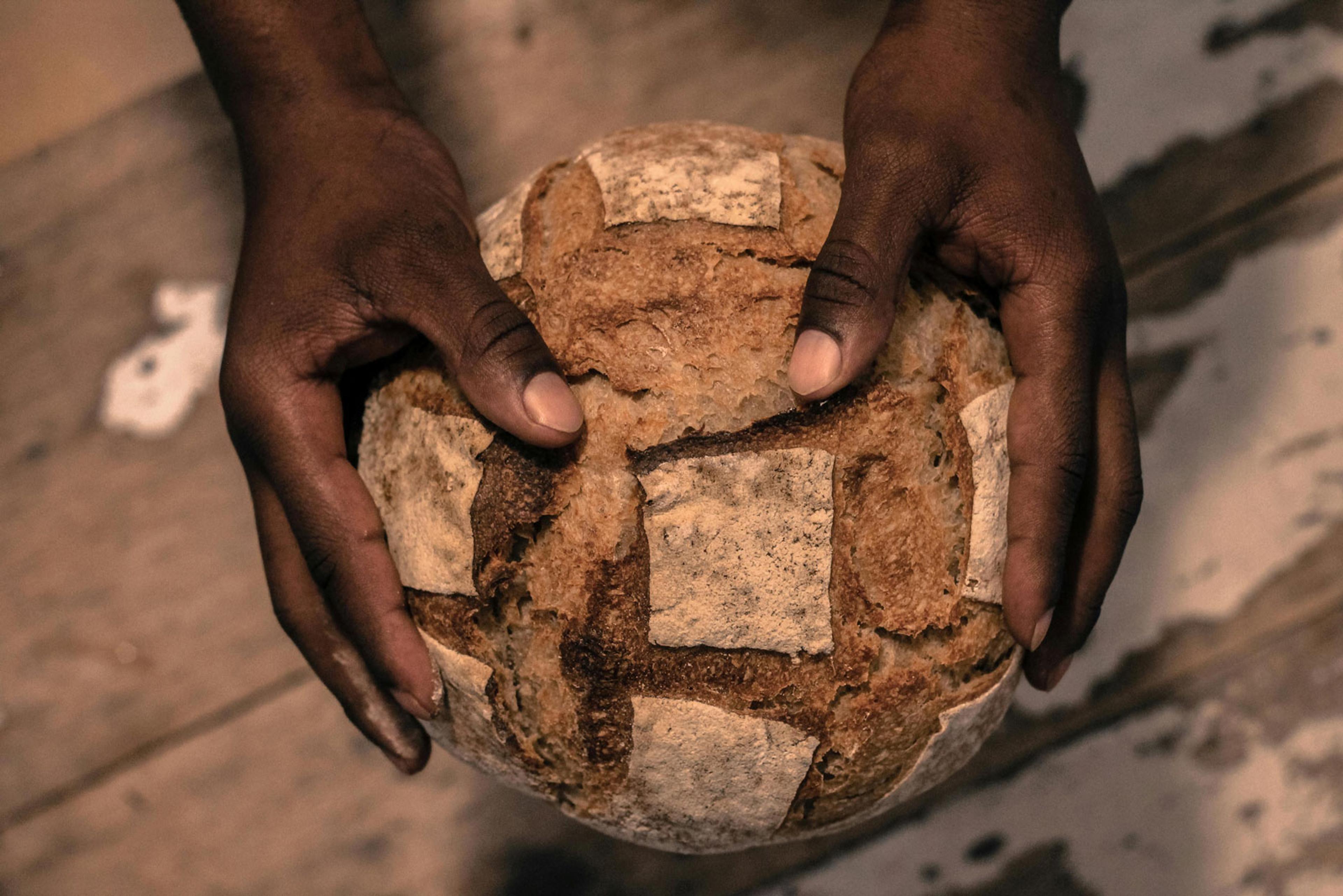 Two hands holding a round loaf of break over a bench.