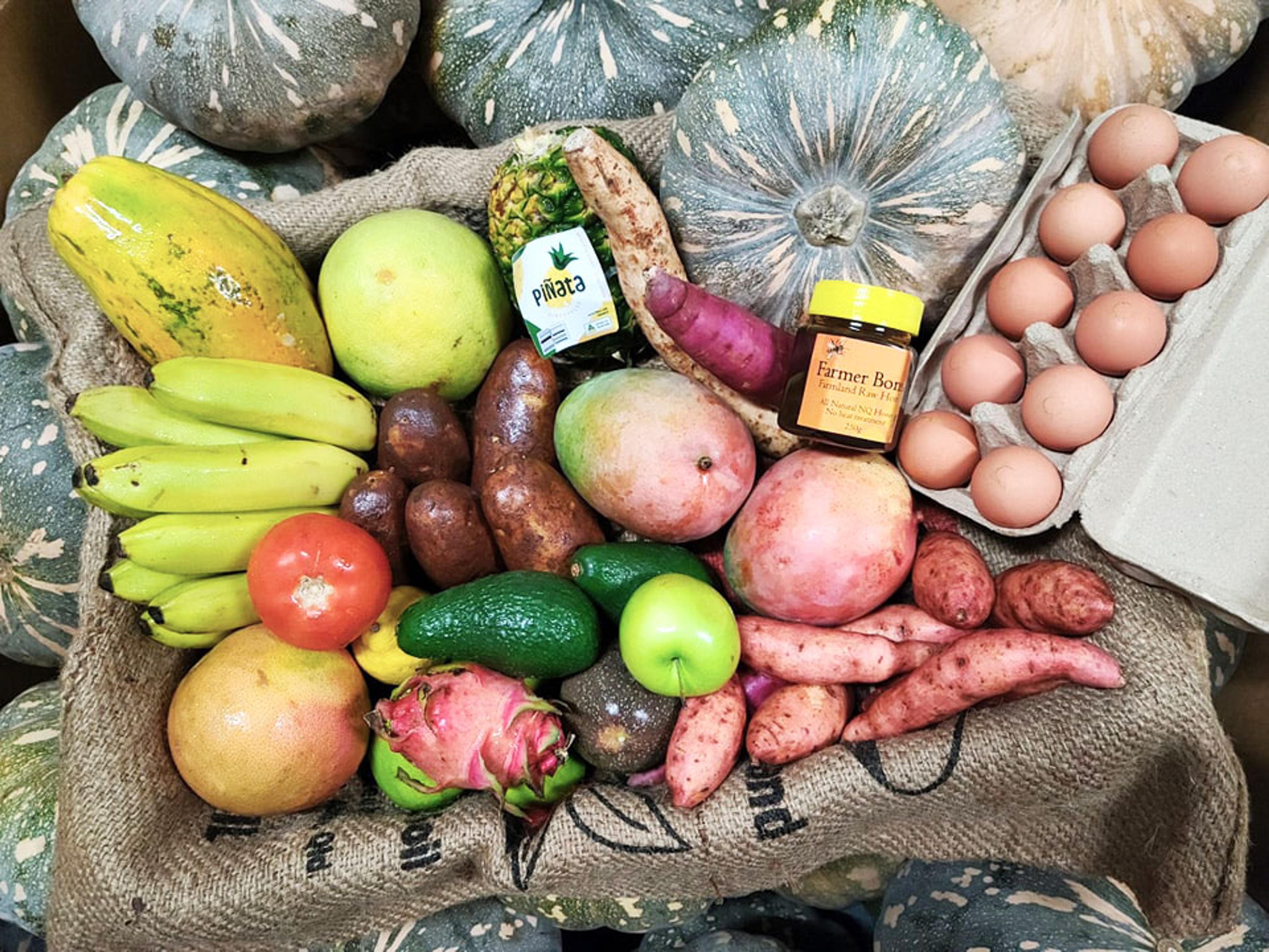 A box of fresh local Far North Queensland produce including pumpkins, bananas, eggs, honey, sweet potato, mango, tomato and more.