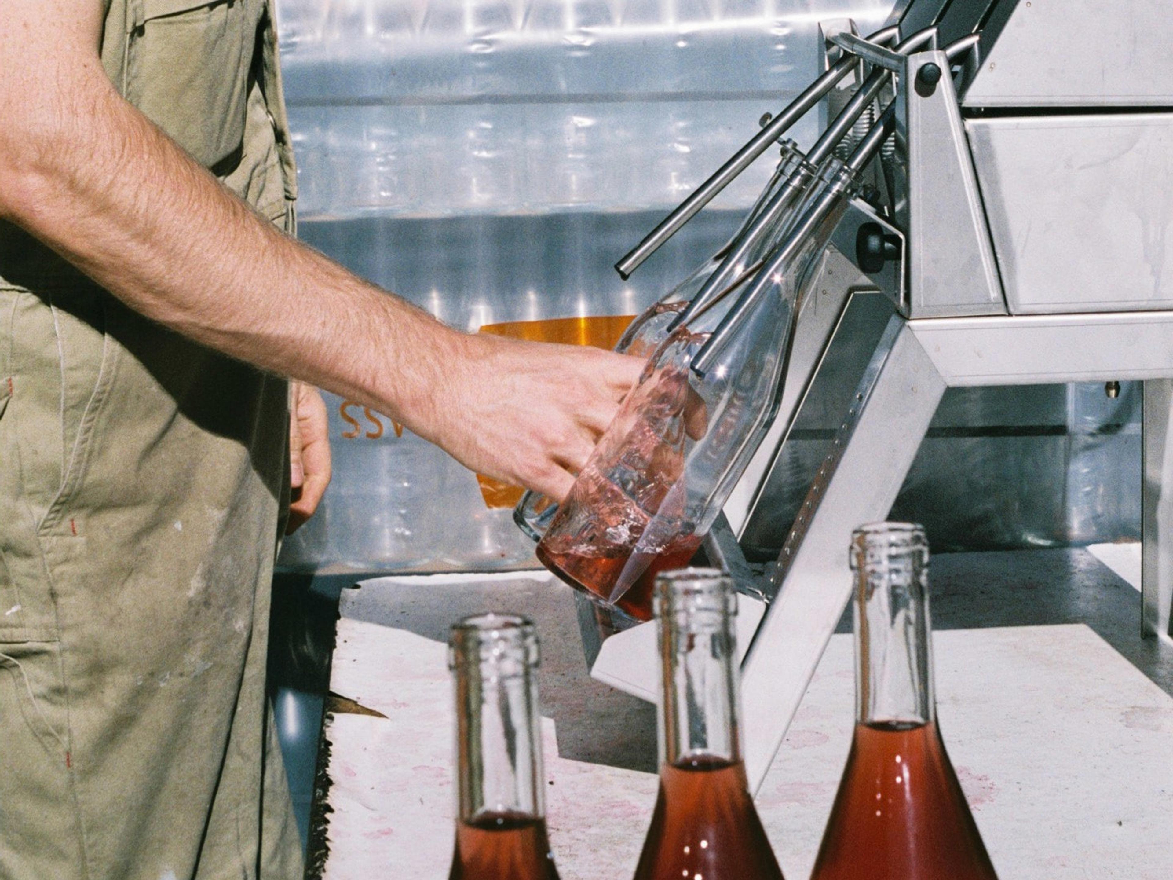 A person bottling wine using a machine.