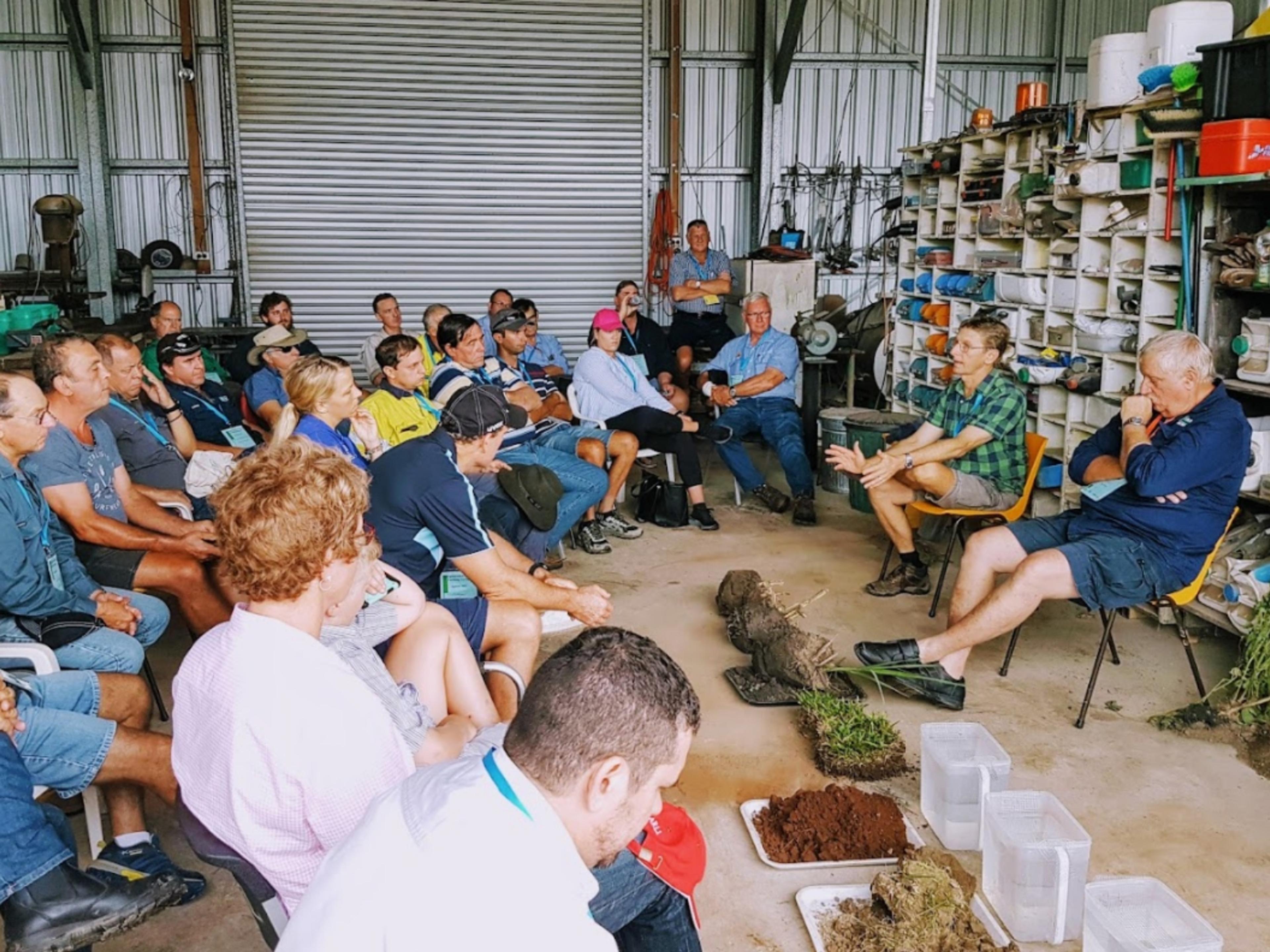 A large group of people in a shed listening intently to a workshop.