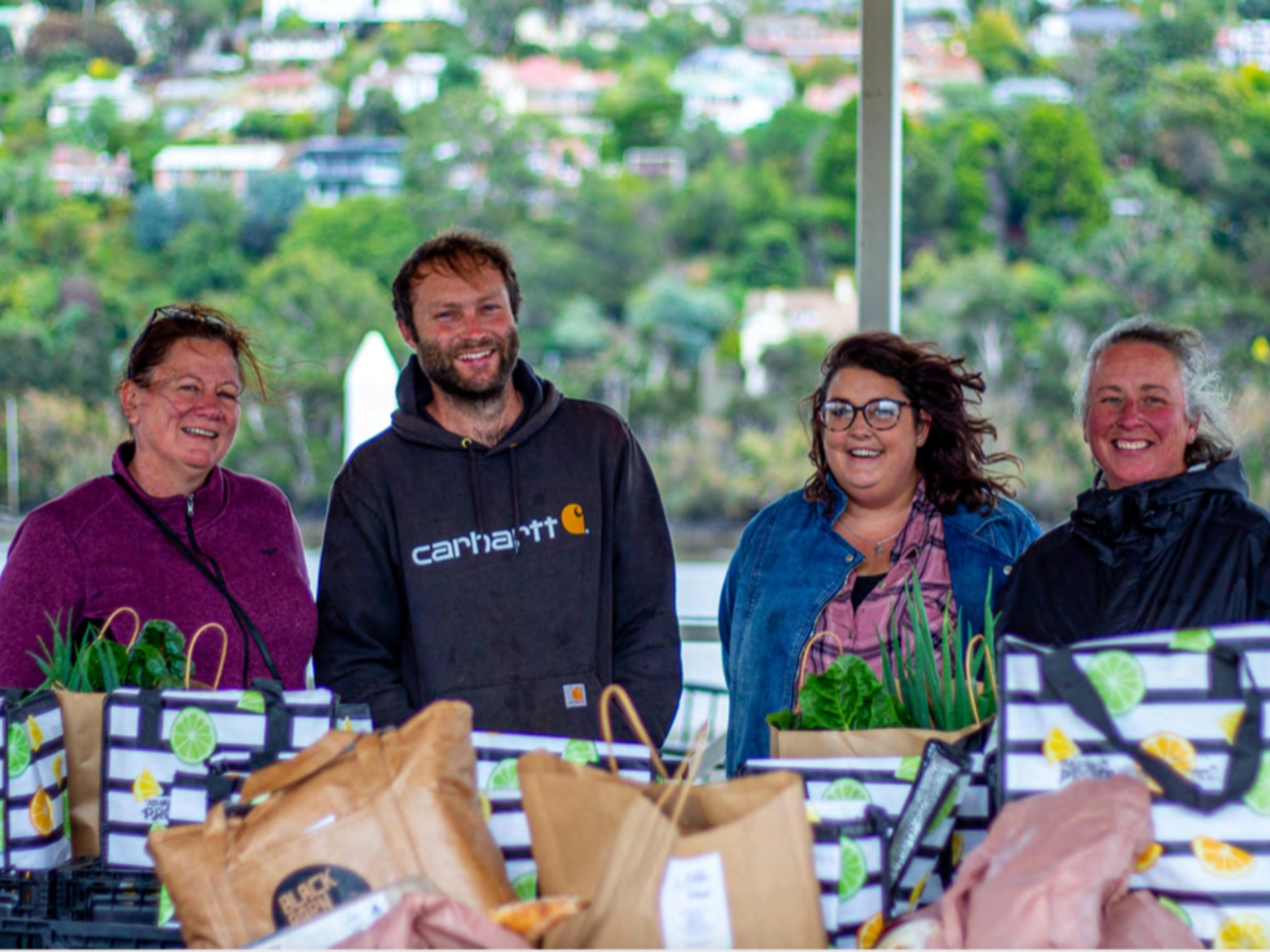 4 people smiling and looking cold in front of paper bags filled with food.