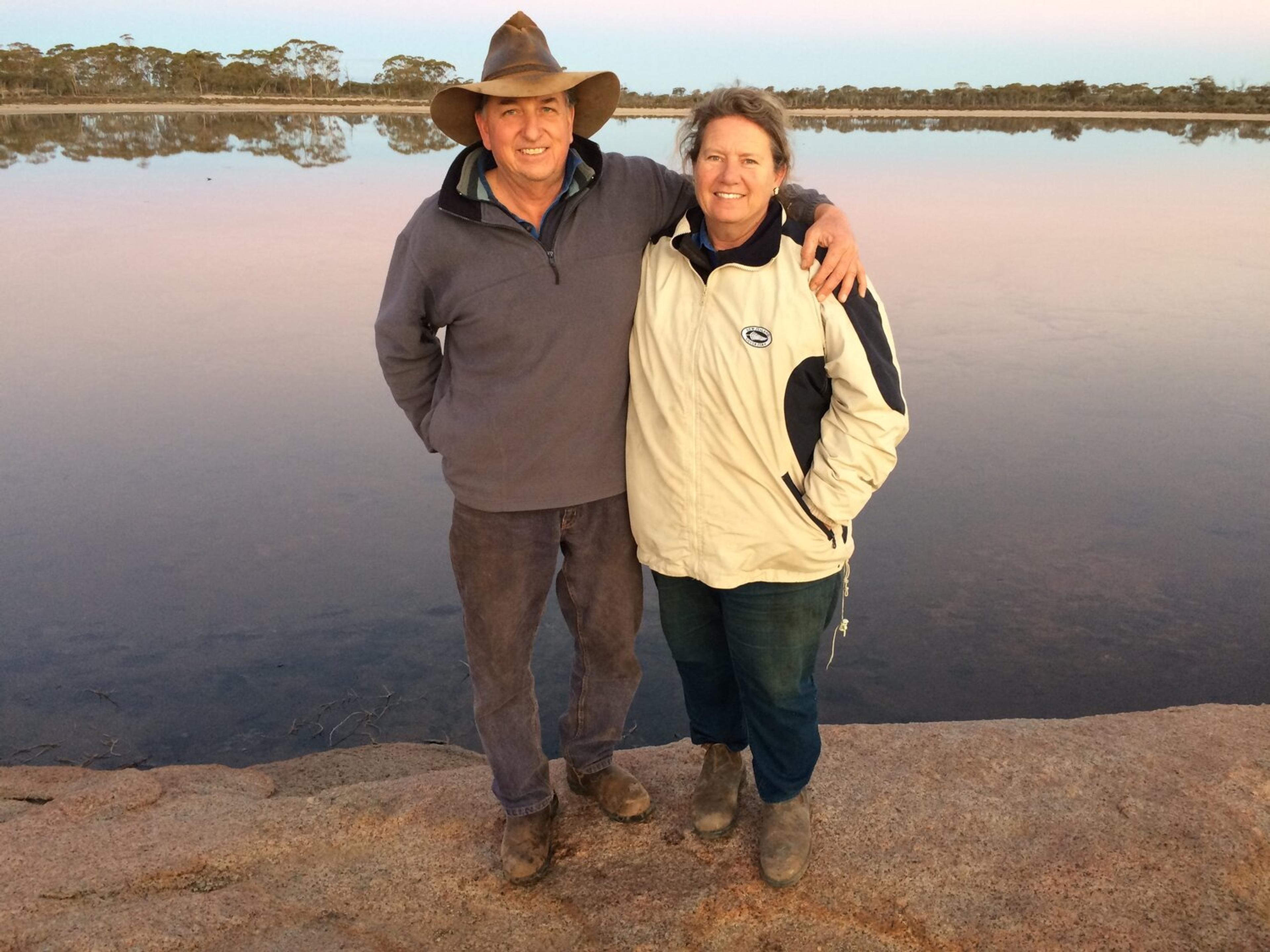 Two smiling farmers standing in front of a body of water. One has their arm around the other.
