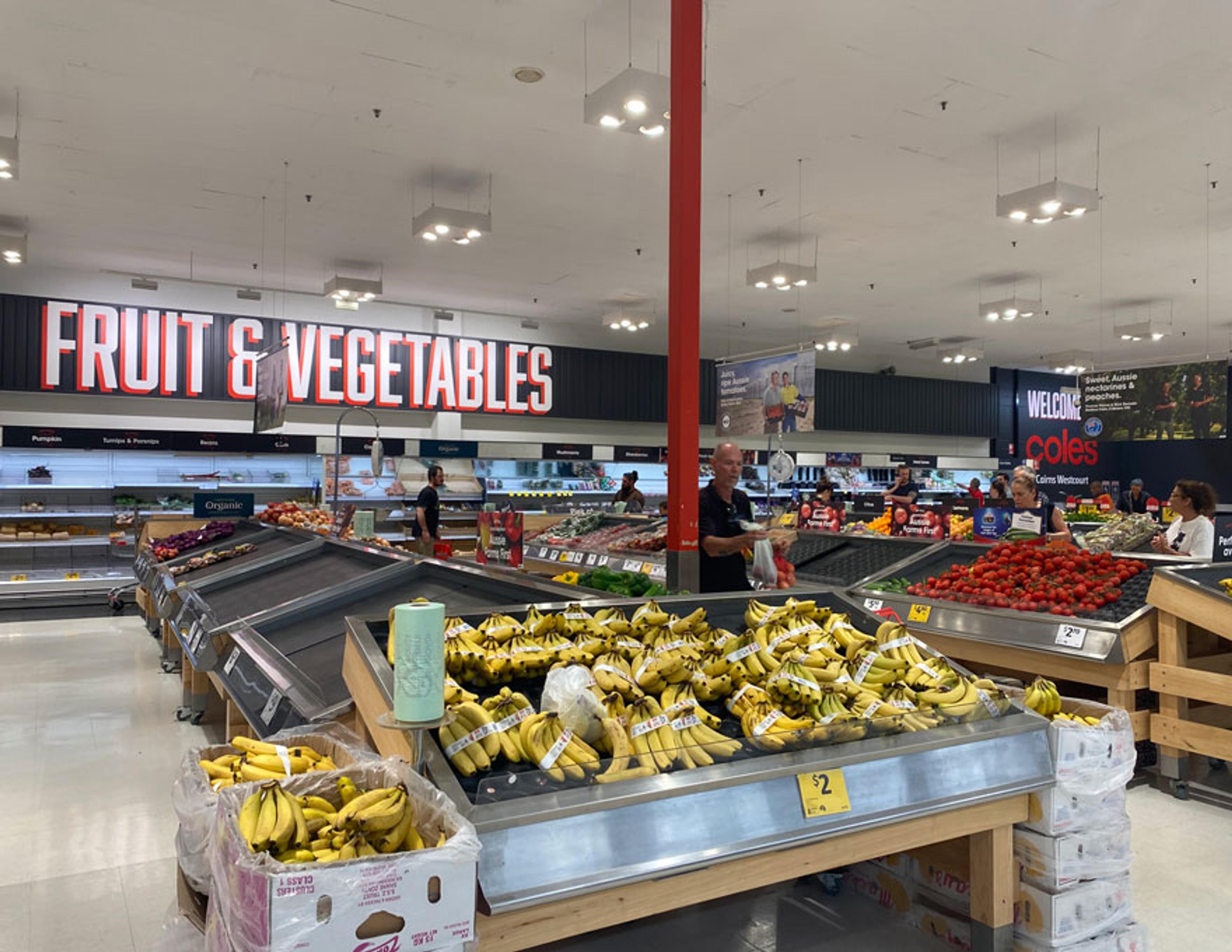 Mostly empty supermarket shelves with some bananas and tomatoes still available.