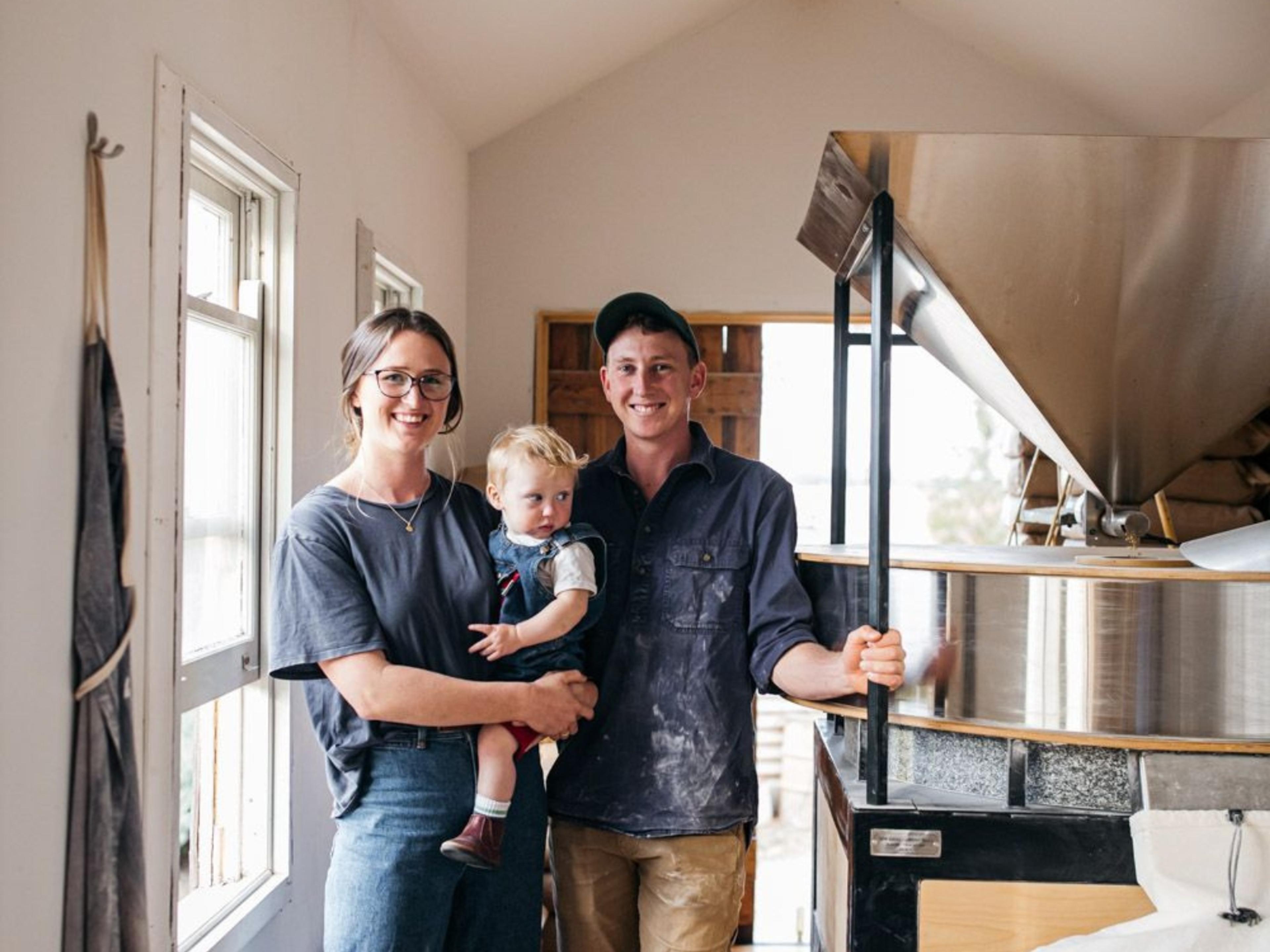 A smiling couple holding their baby next to a flour sifter.