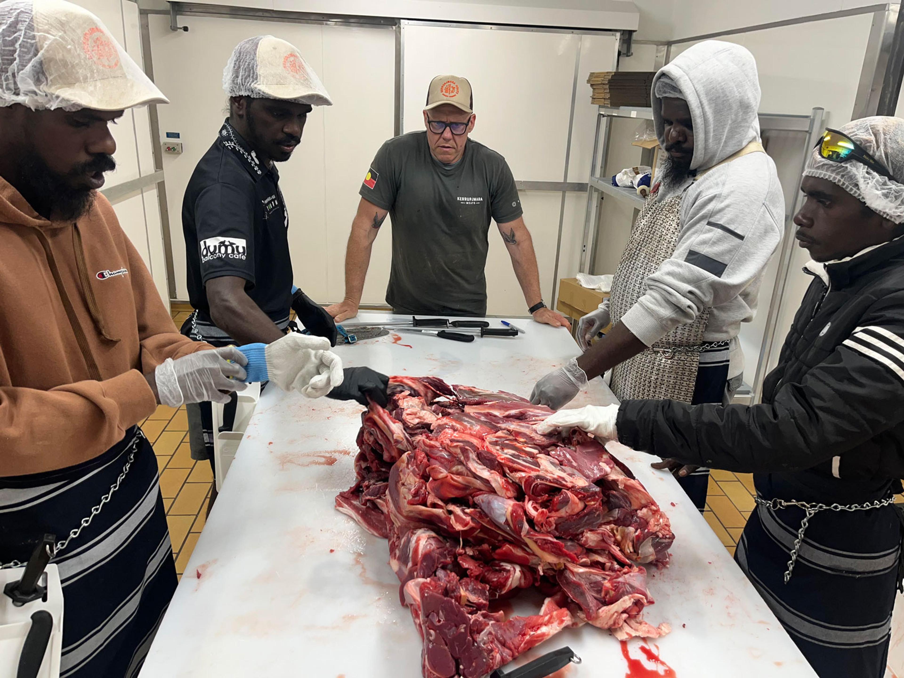 5 men standing standing around a table butchering a piece of meat.