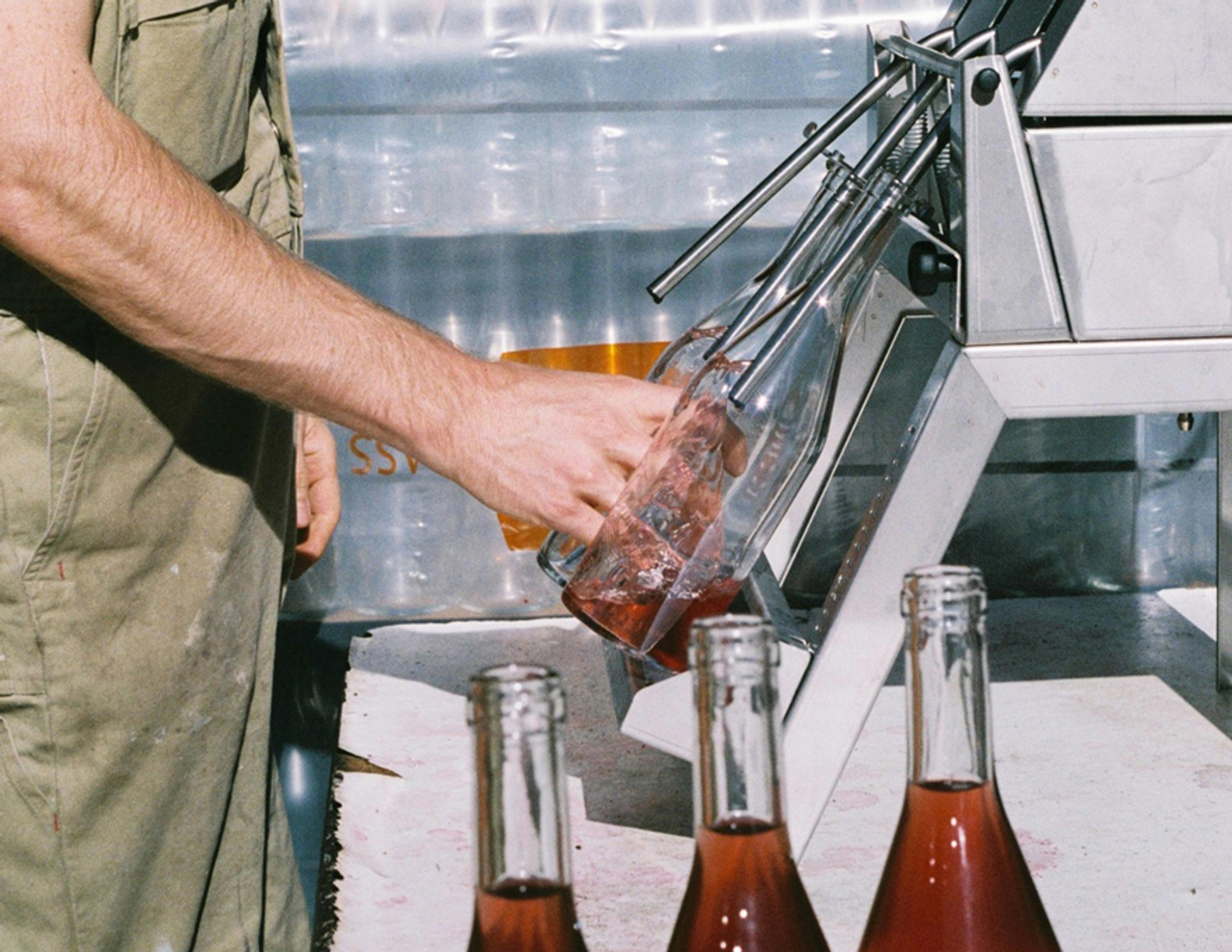 A person bottling wine using a machine.