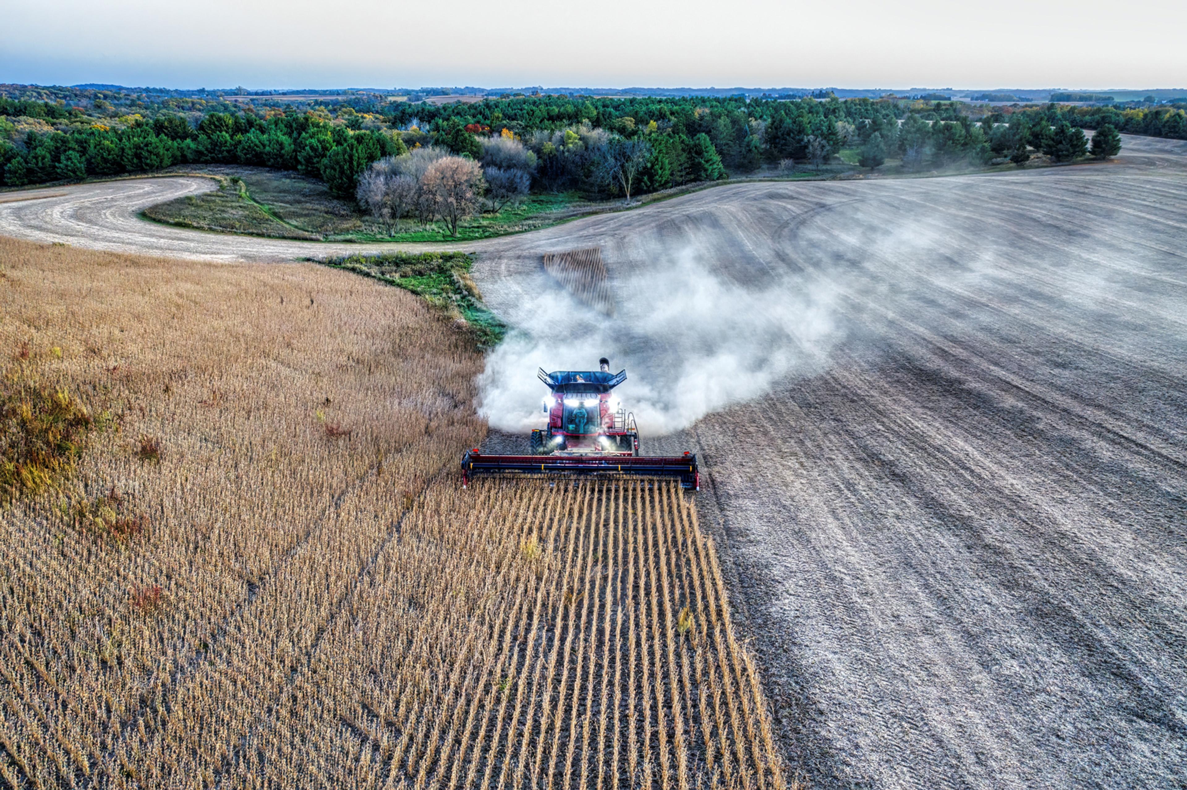 A machine harvesting crops. One side of the field is already harvested and is a dark brown colour, the other side is still yet to be harvested.