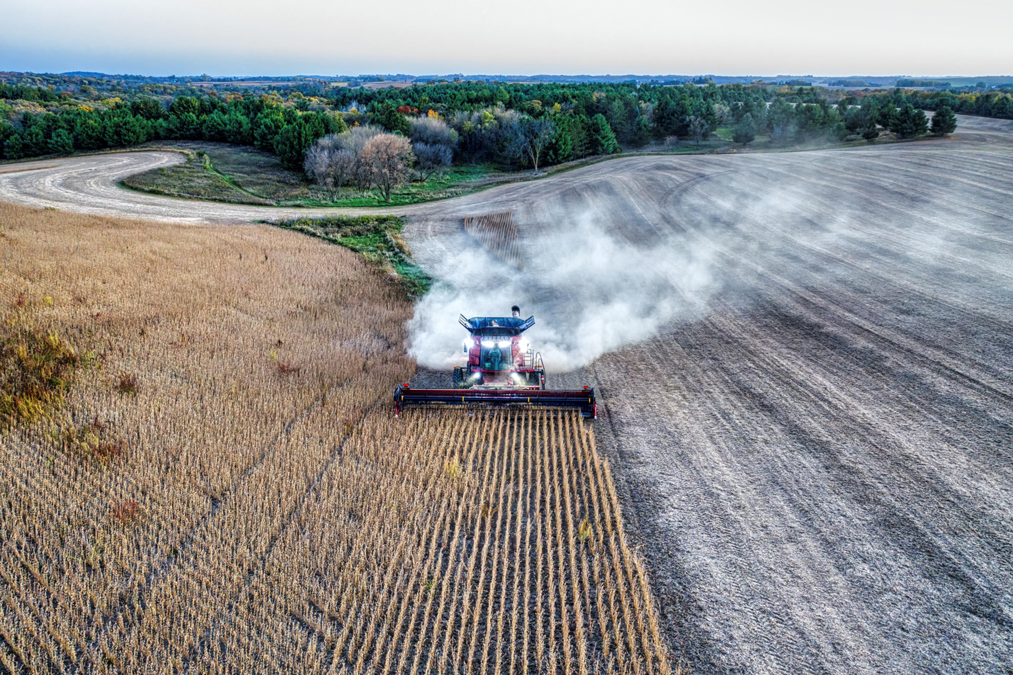 A machine harvesting crops. One side of the field is already harvested and is a dark brown colour, the other side is still yet to be harvested. 