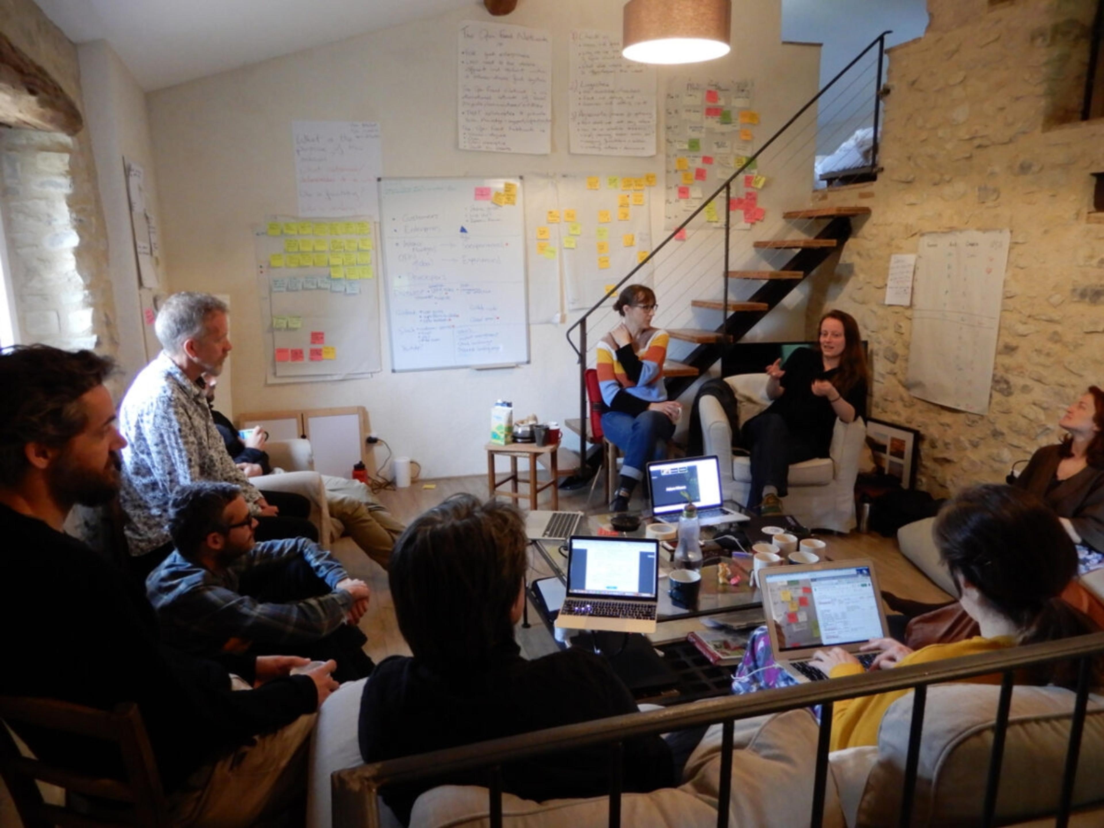 A group of people sitting in a room with paper and post it notes all over the walls and laptops open.