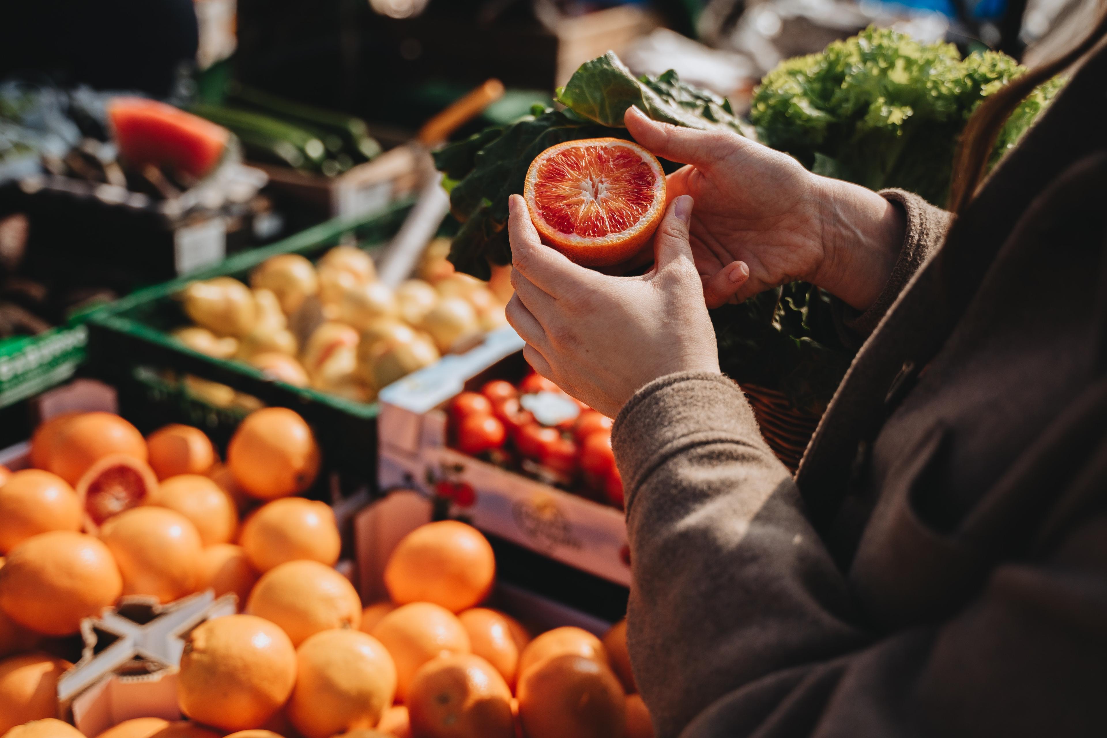 A person inspecting a blood orange in front of crates of different fruits