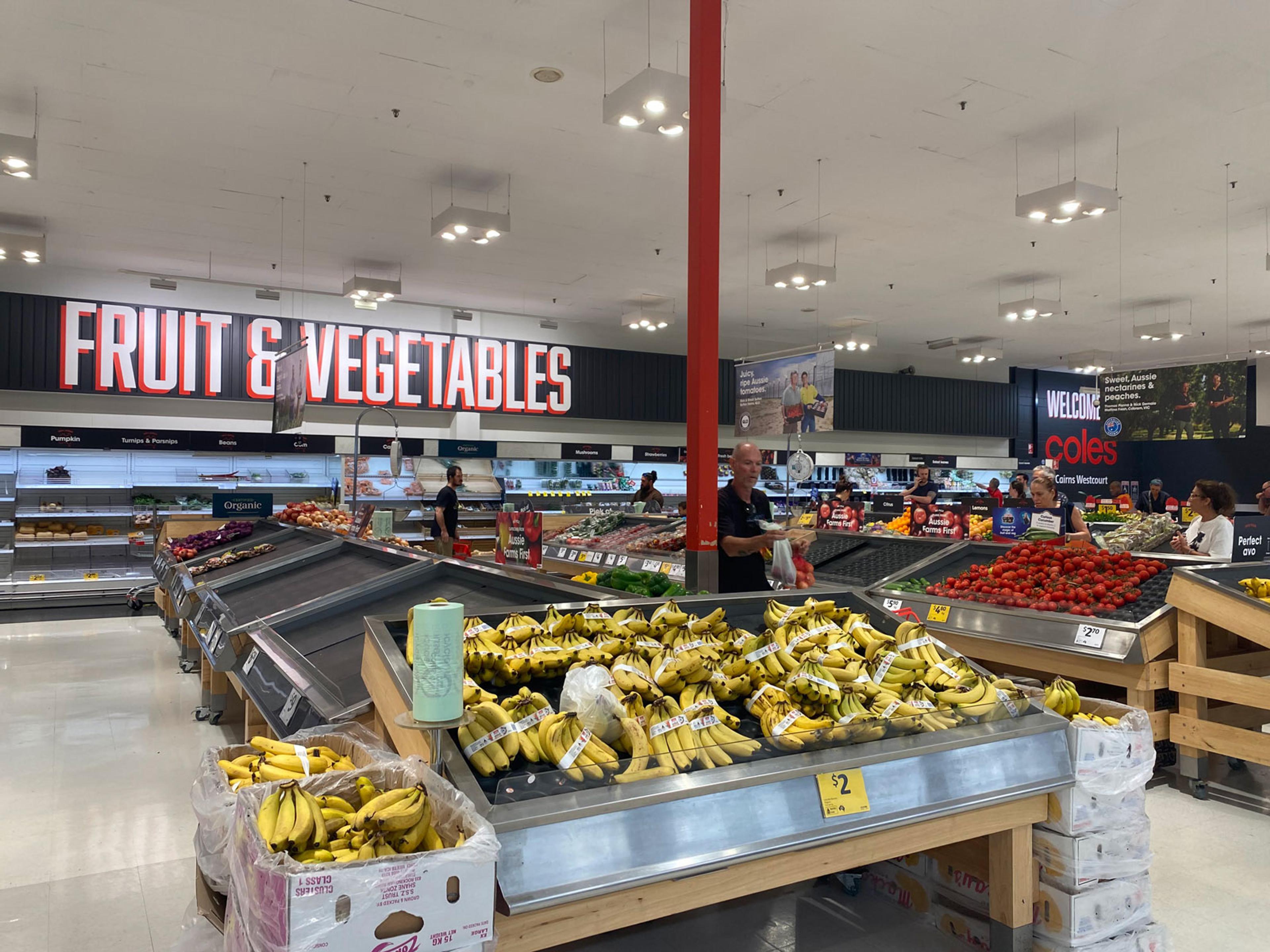 Mostly empty supermarket shelves with some bananas and tomatoes still available.