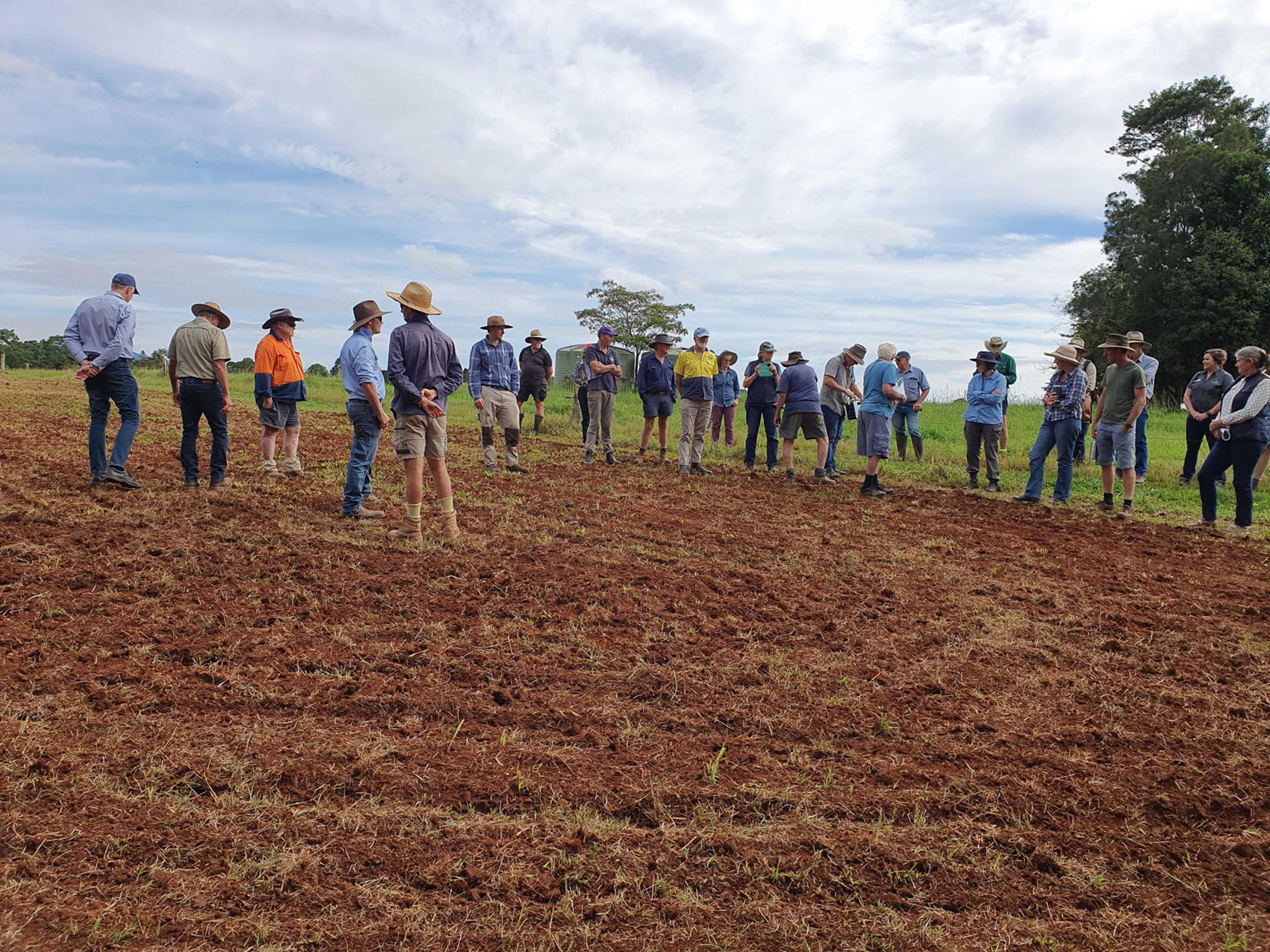 A group of farmers standing around in a dirt paddock that has not been planted.