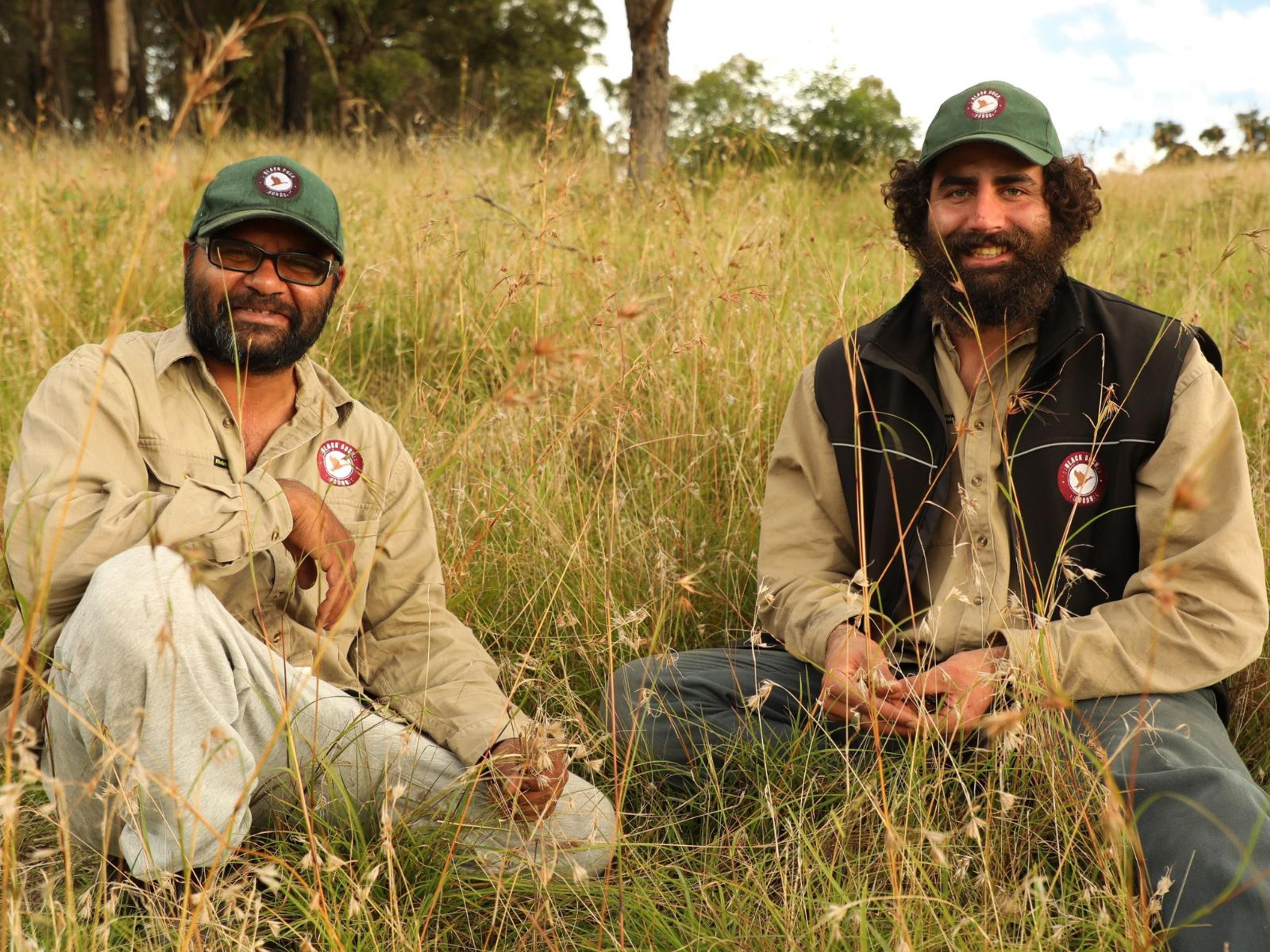 Two people sitting in a field of native grasses.