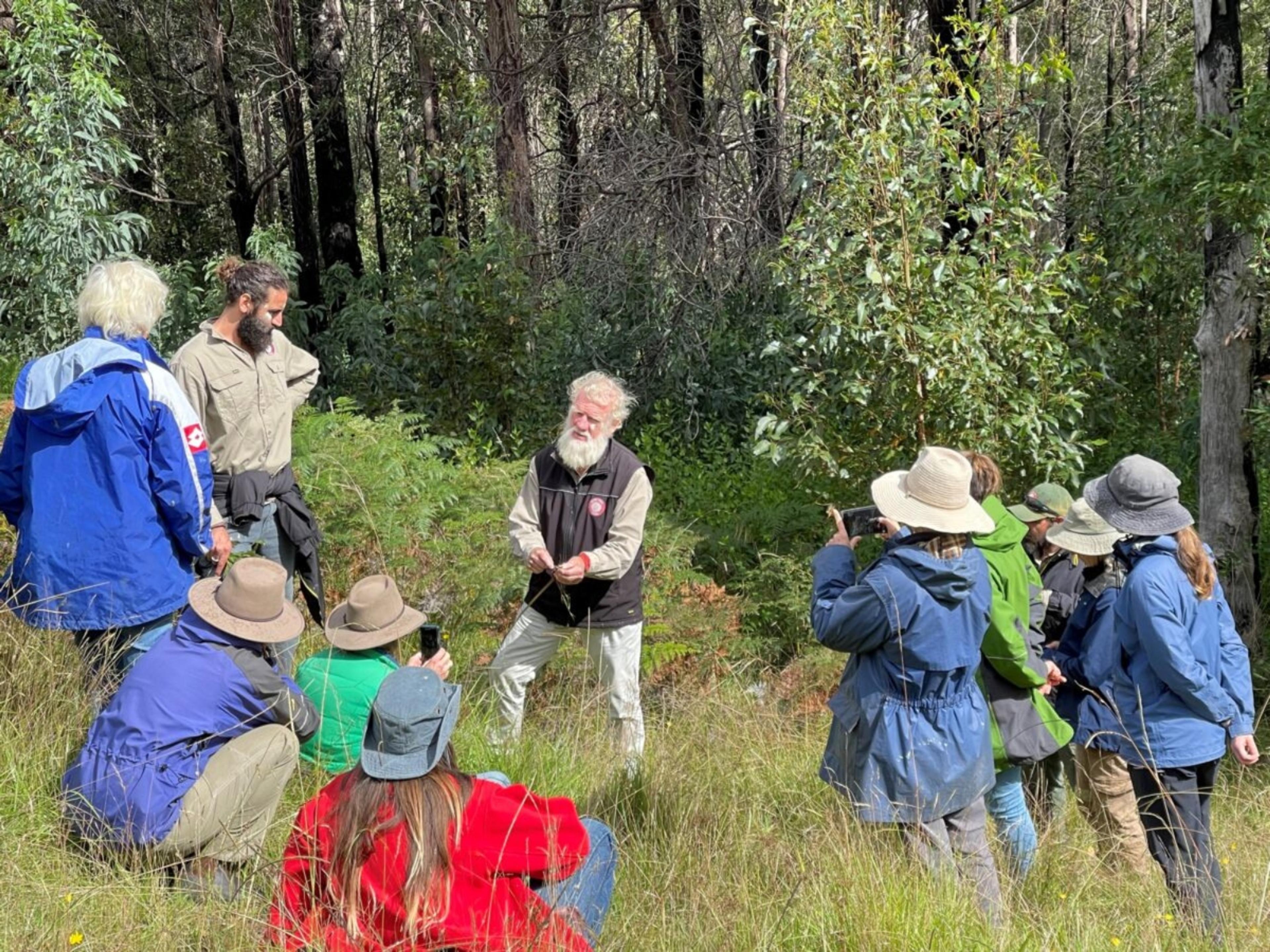 A group of people out in nature listening to Bruce Pascoe speak.