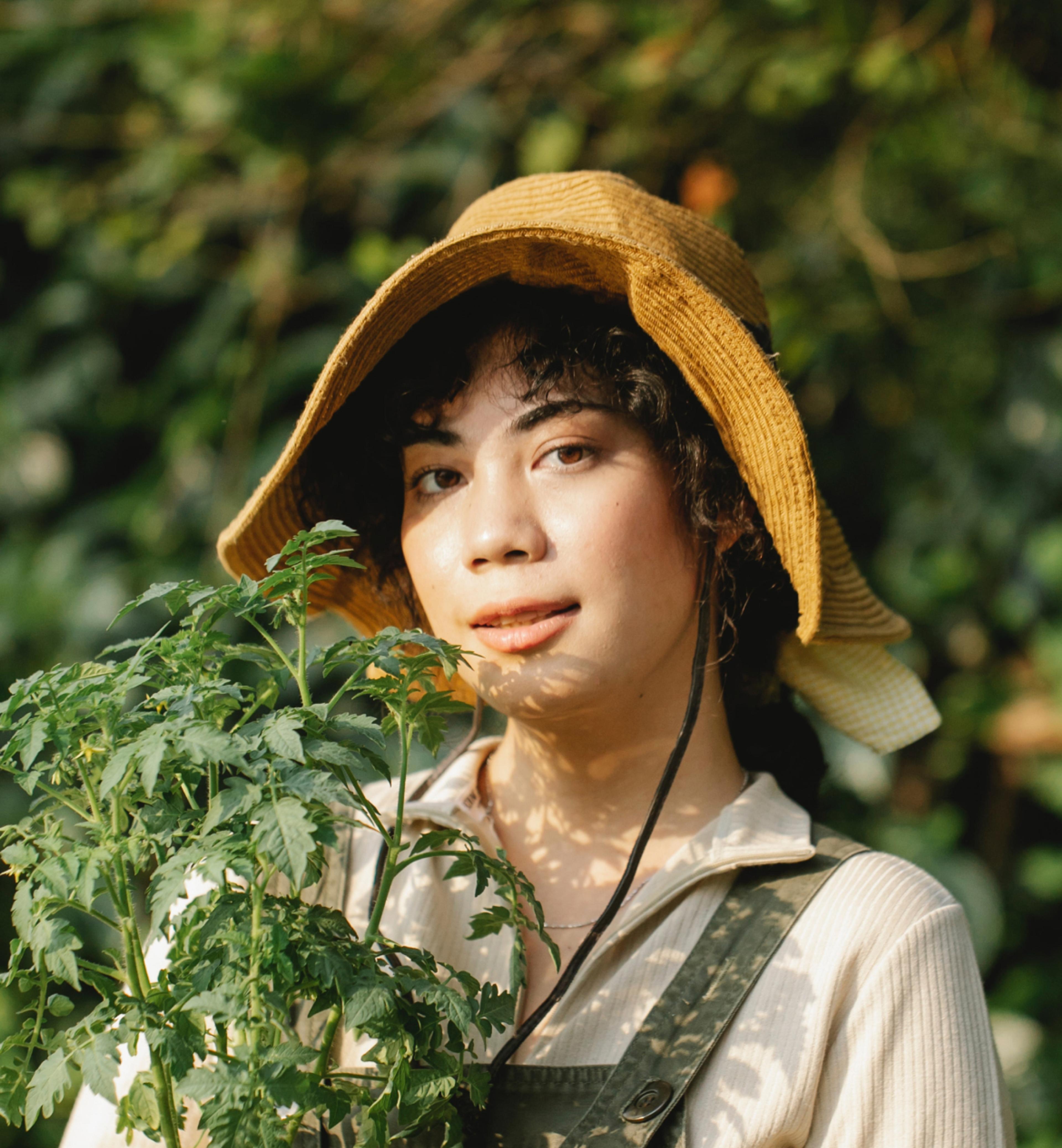 Woman with a hat holding a plant in a terracotta pot.