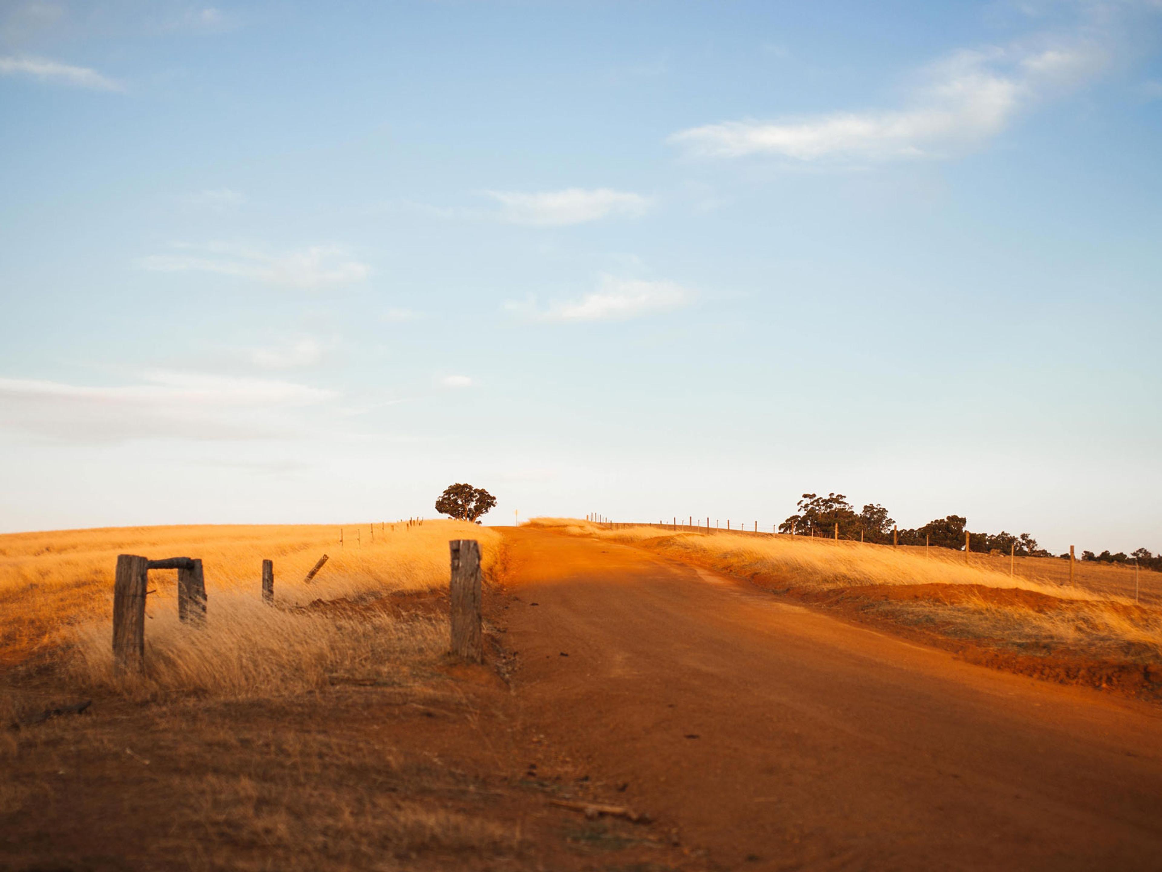 A dusty red road. There are blue skies with small cloud overhead. 