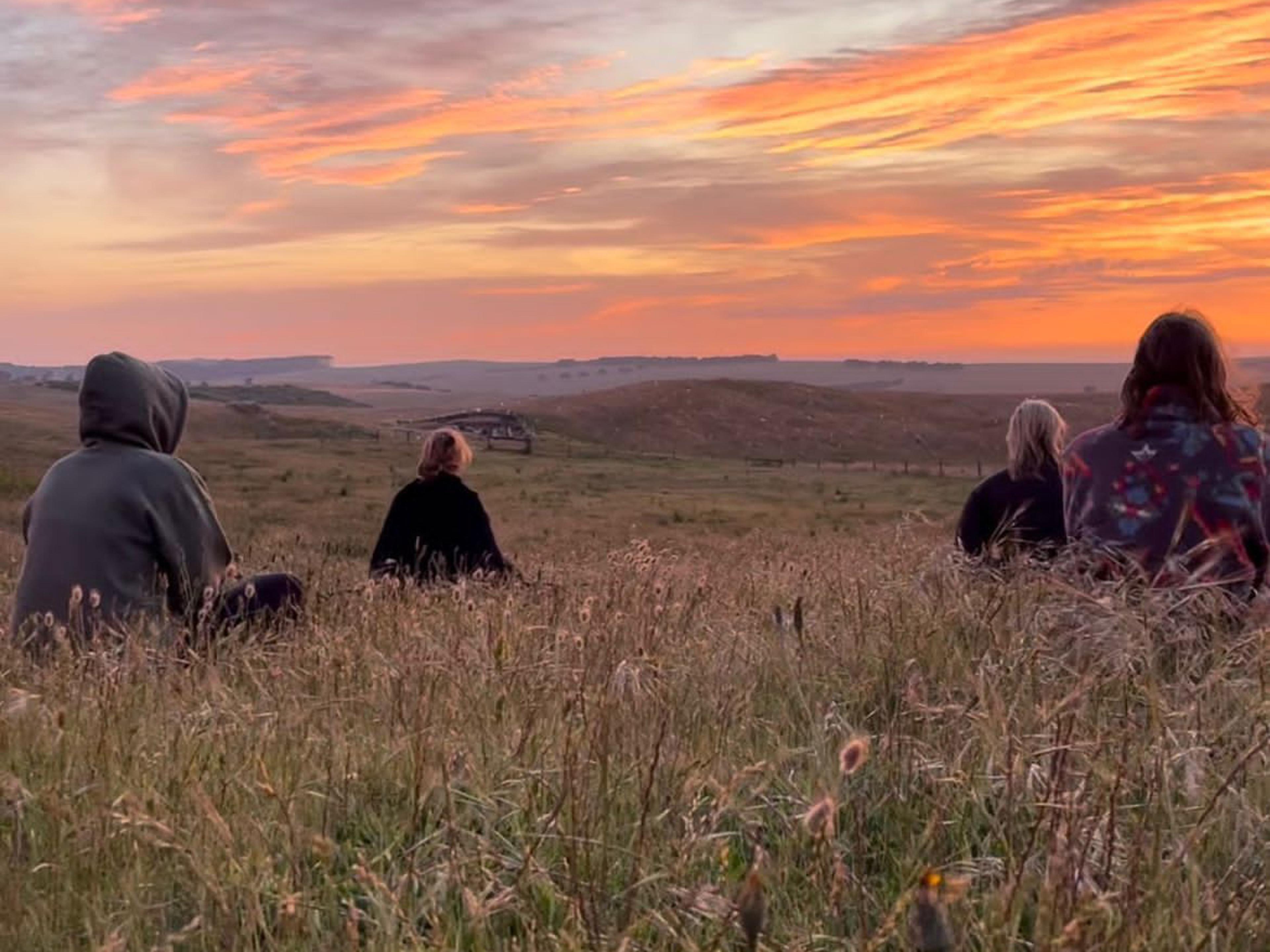 A group of women sitting in a field watching the sunrise