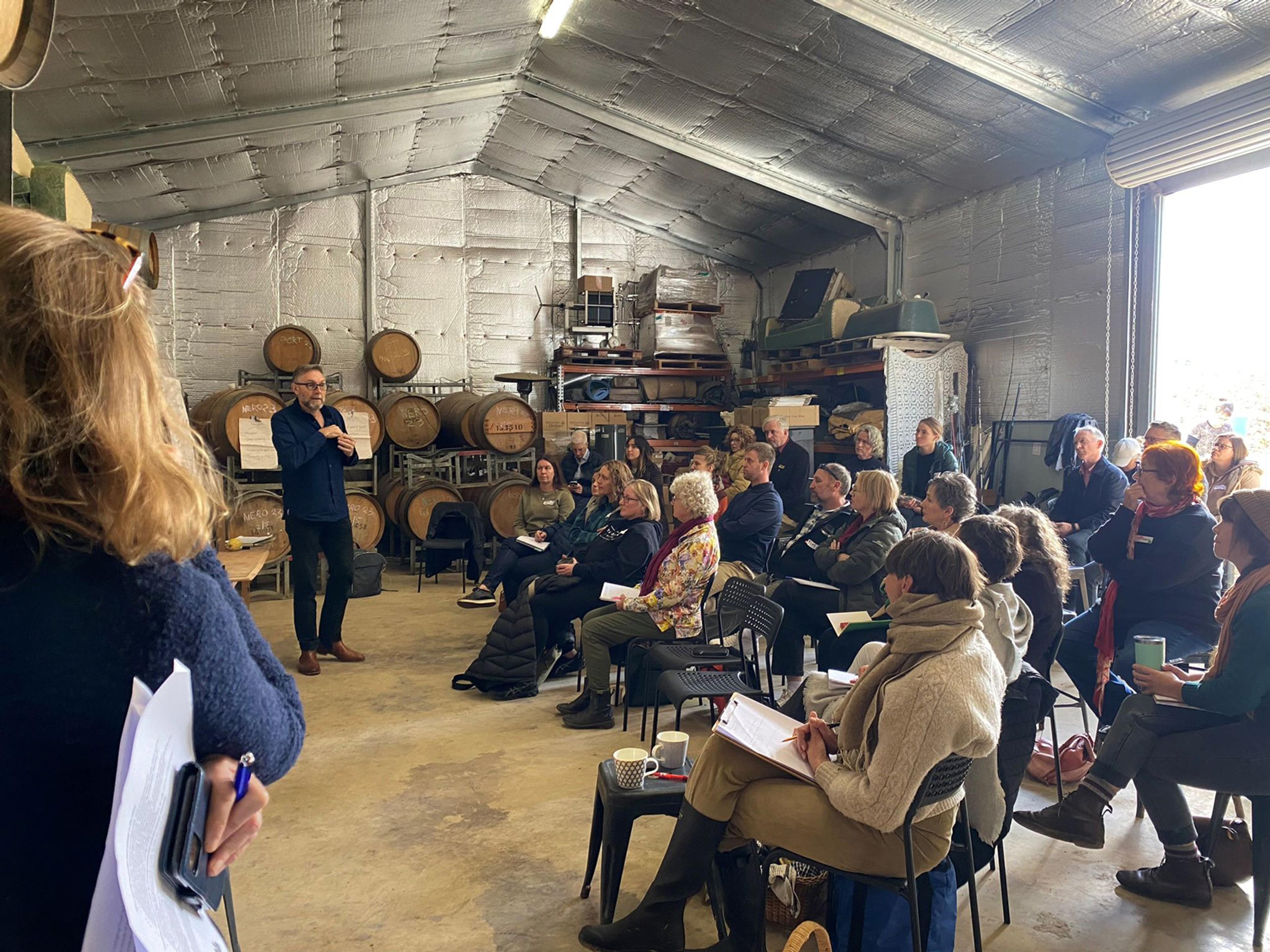 A group of people listening to a speaker in a farm shed.