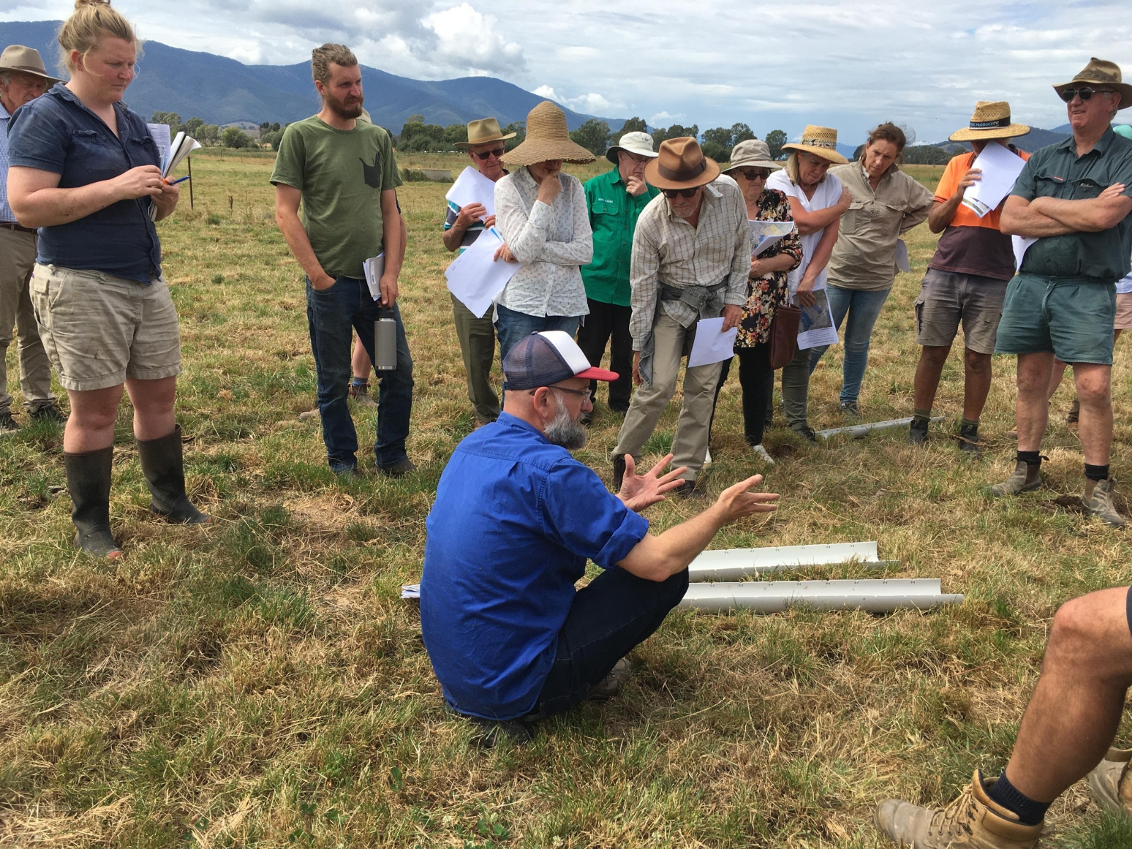 A small group of people in a field listening to someone delivering a workshop.