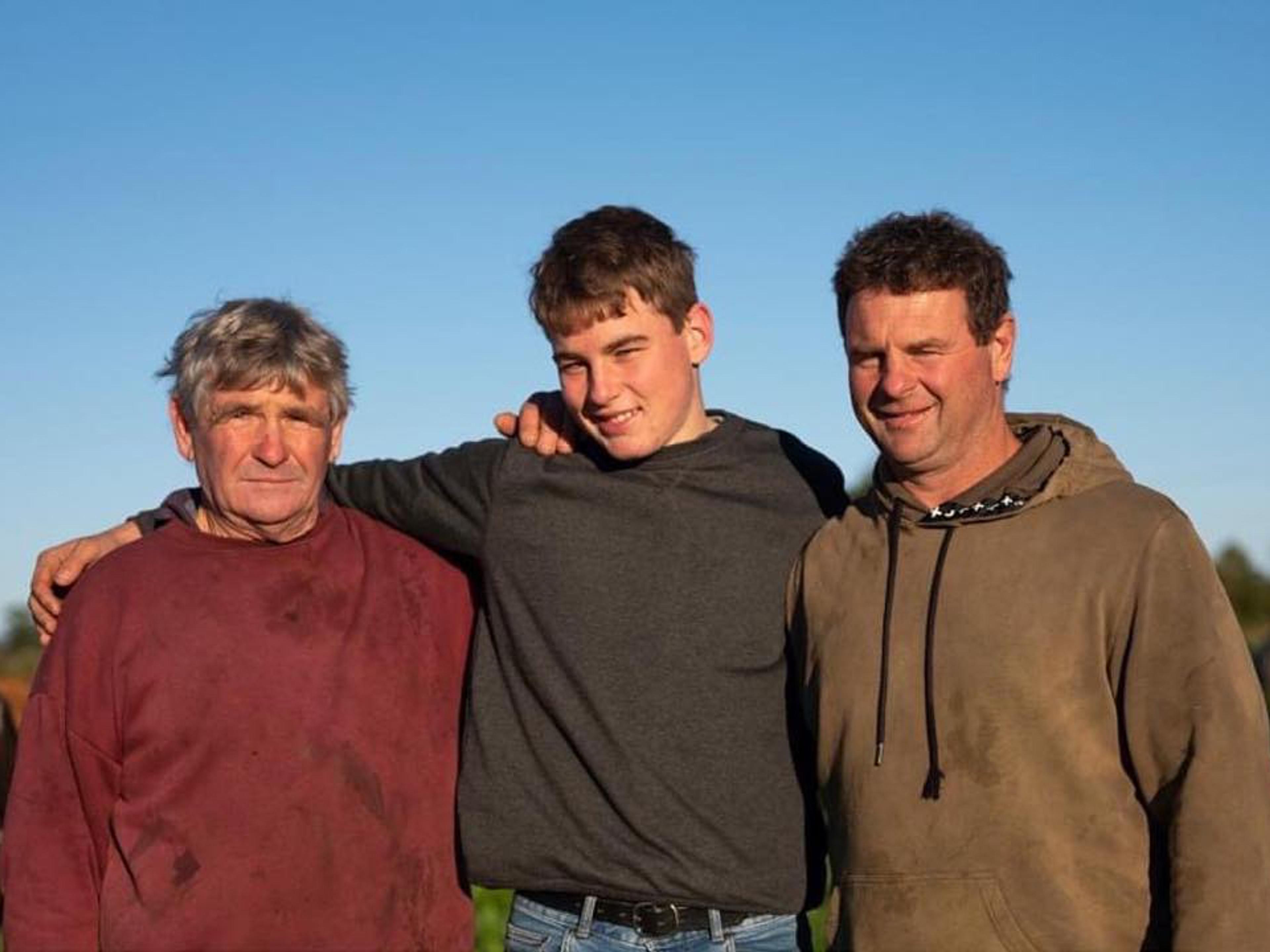 3 generations of farmers staring into the camera with blue skies behind them.