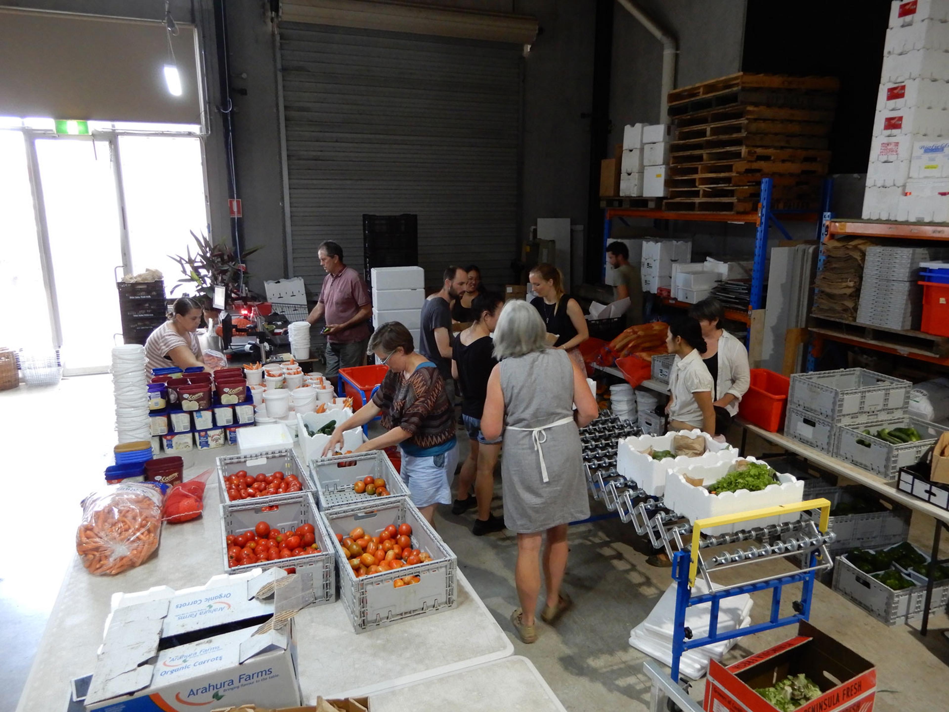A group of people in a big shed with tables full of fresh produce. It looks as if they are organising the produce.