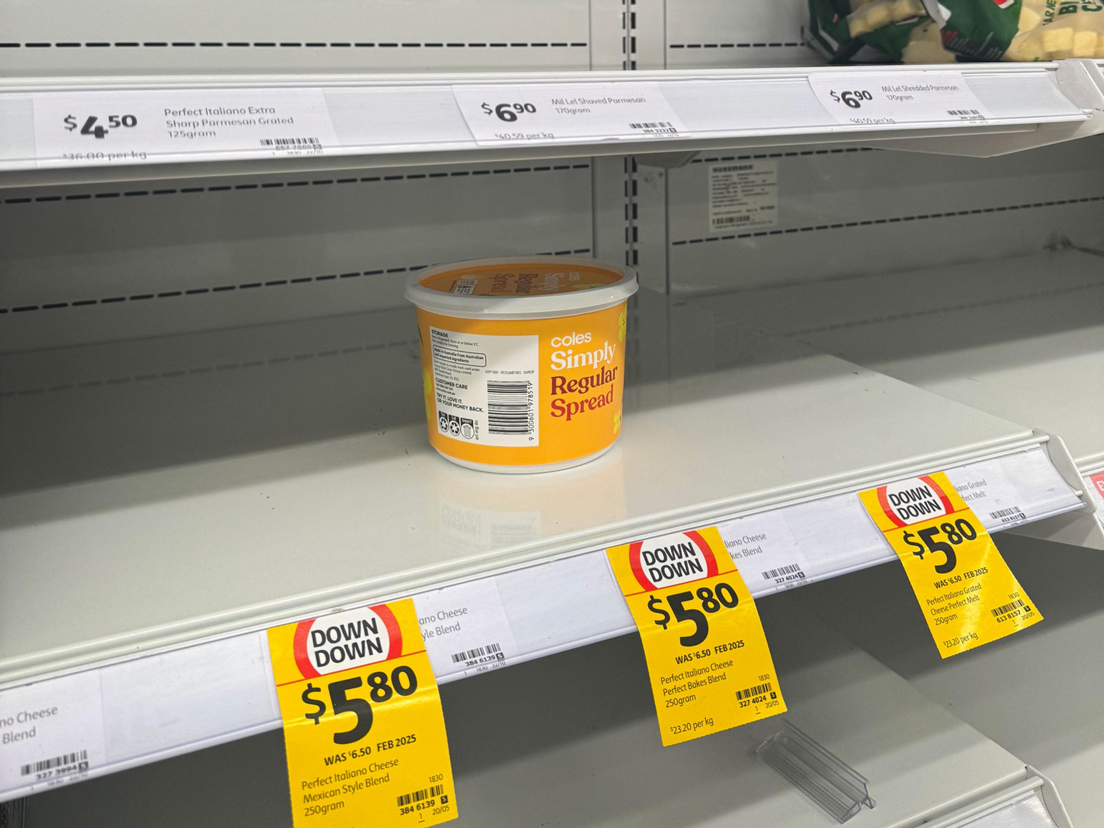 An empty supermarket fridge shelf with a single tub of margarine on it.