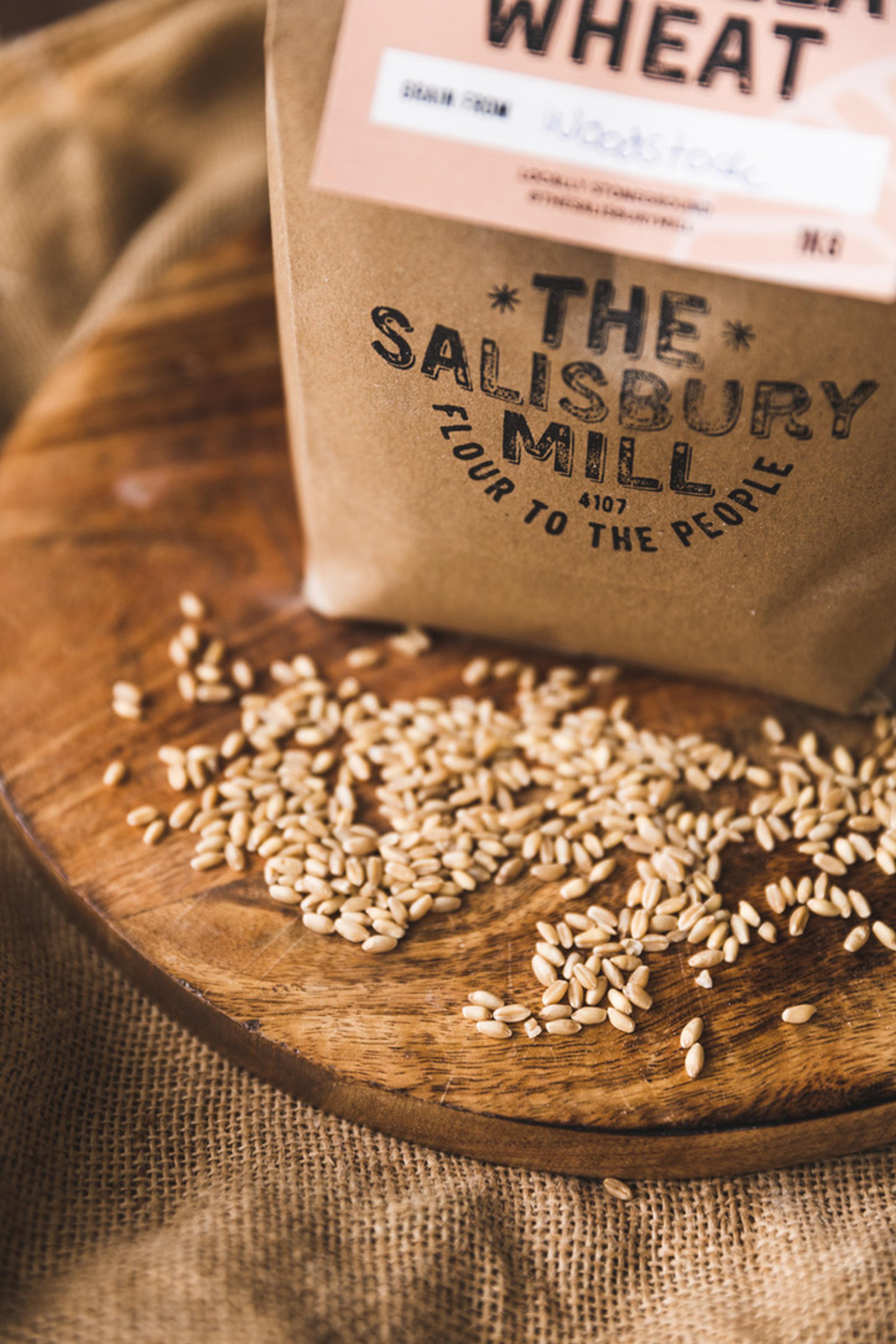 A bag of flour and some grains laid out on a table in front of it.