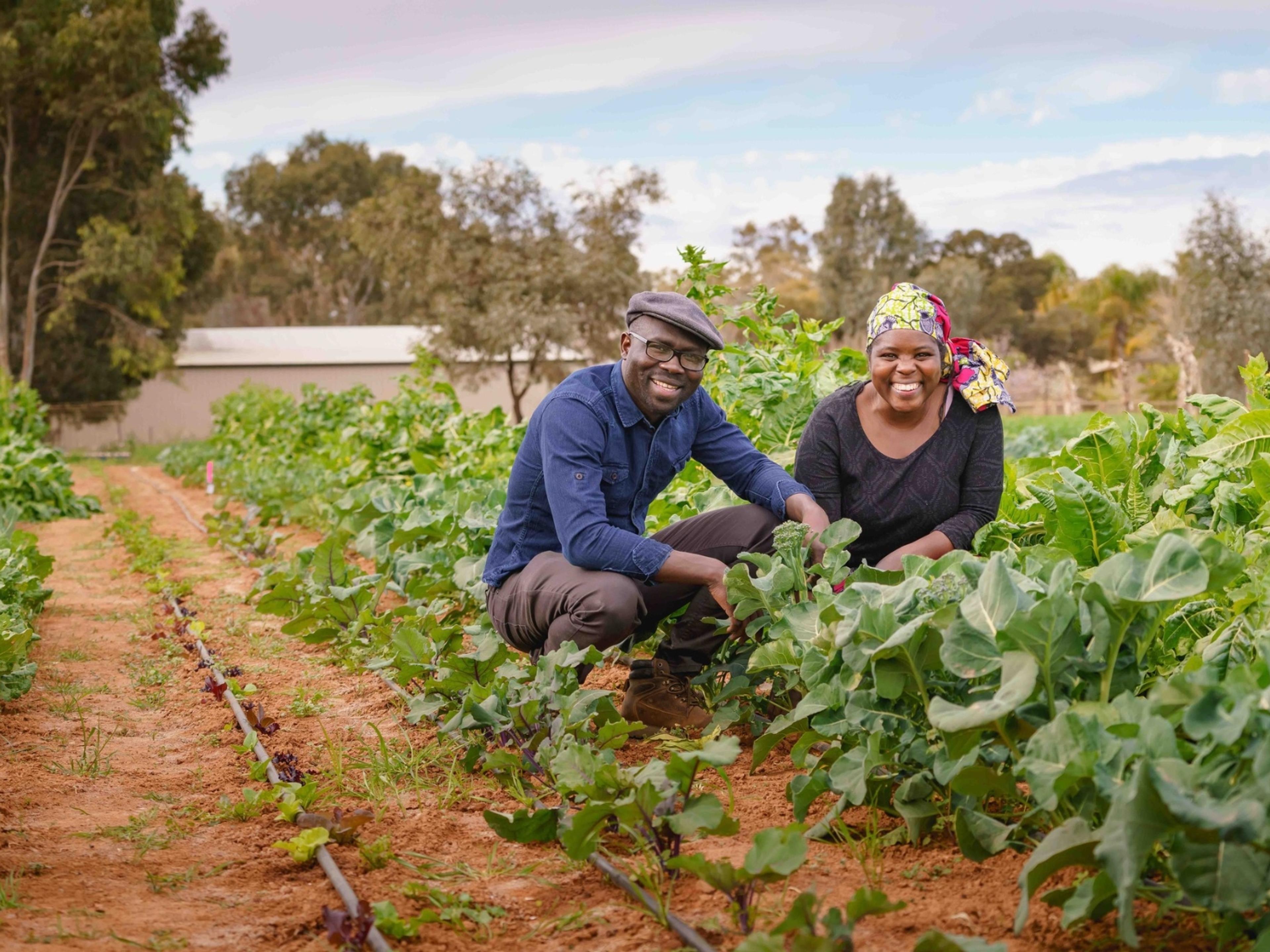 Two people smiling in a field of growing plants. It's a sunny day.