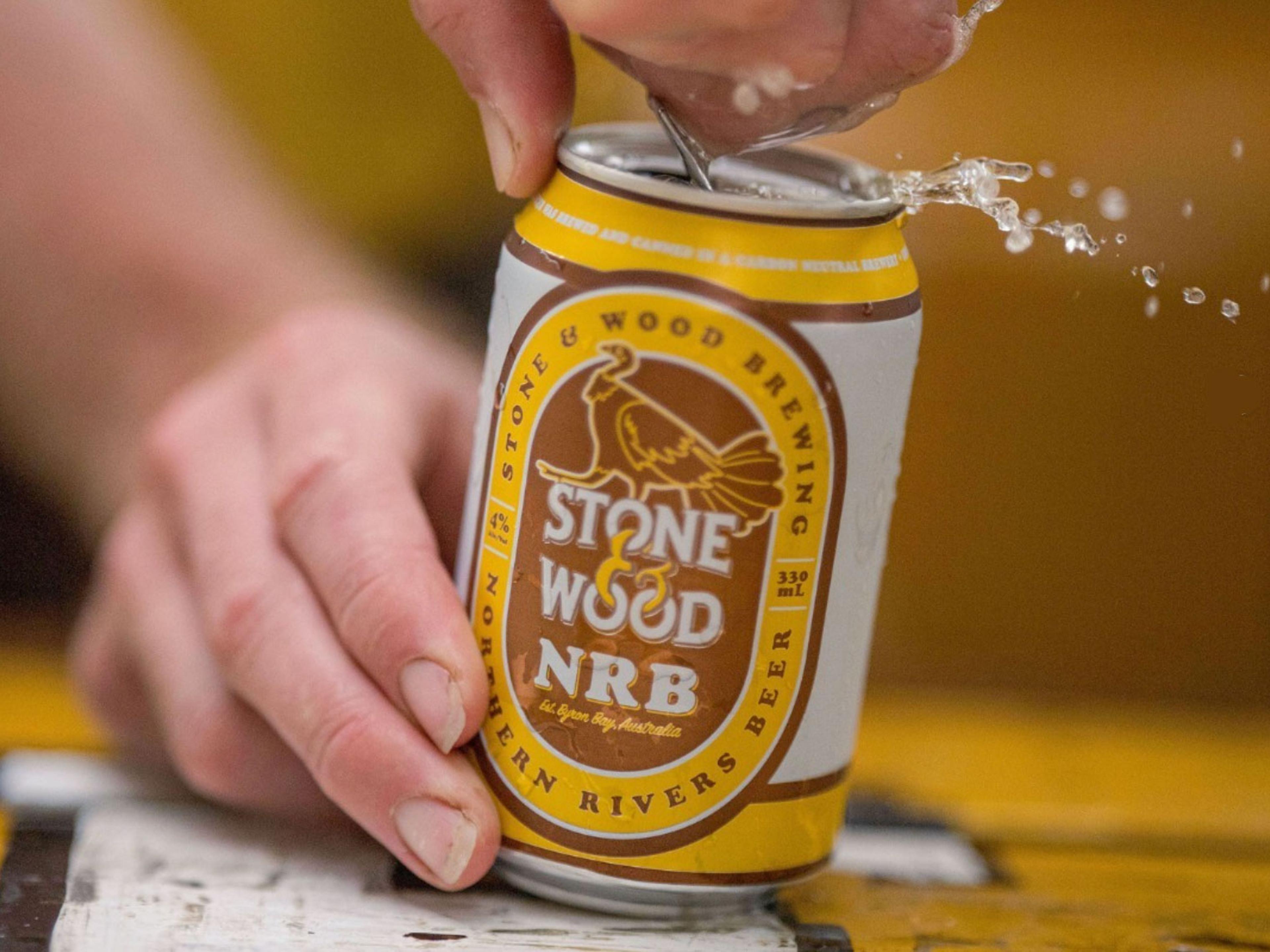 A hand opening a yellow, white and brown can of Stone & Wood's Northern Rivers Beer.