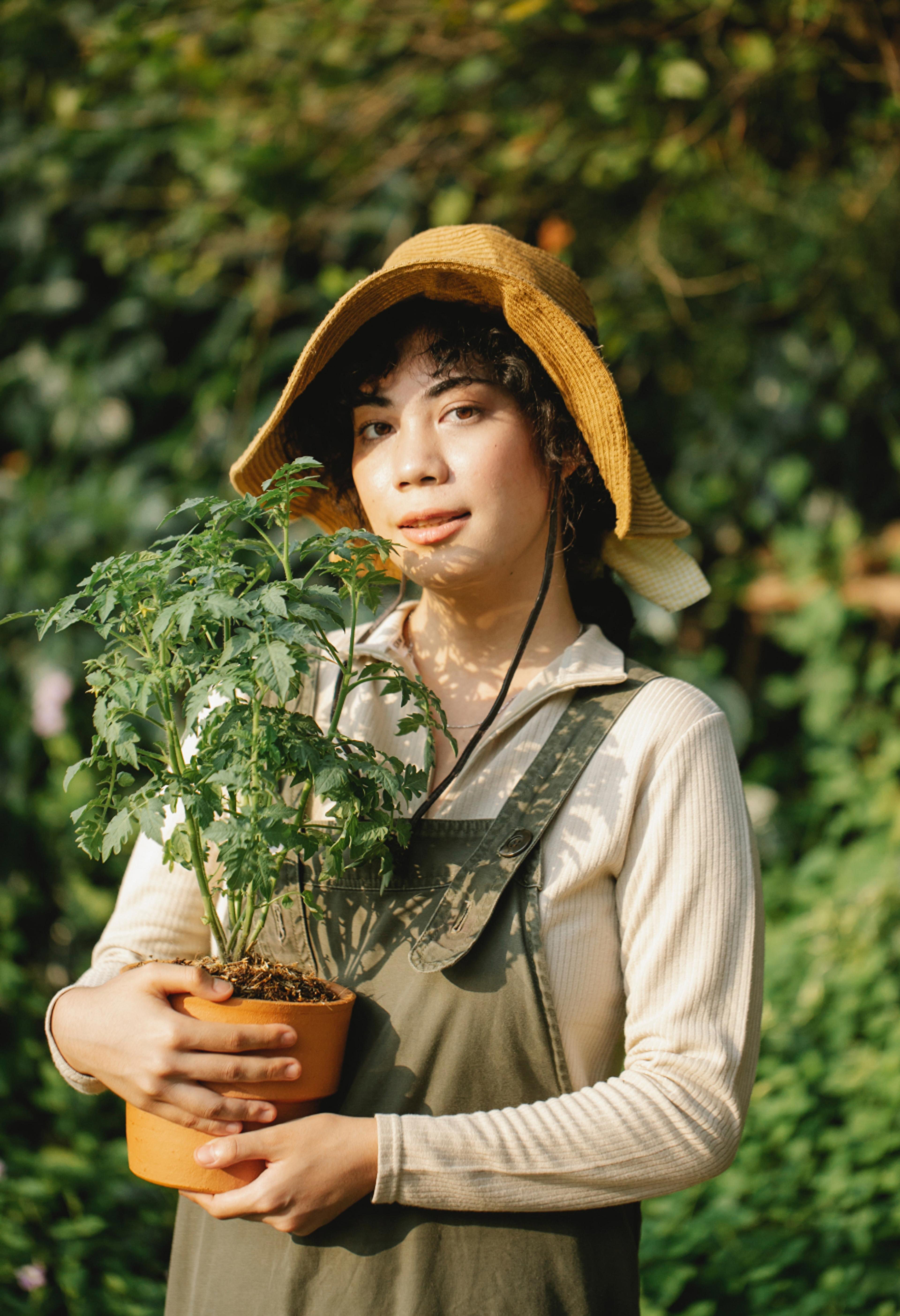 Woman with a hat holding a plant in a terracotta pot.