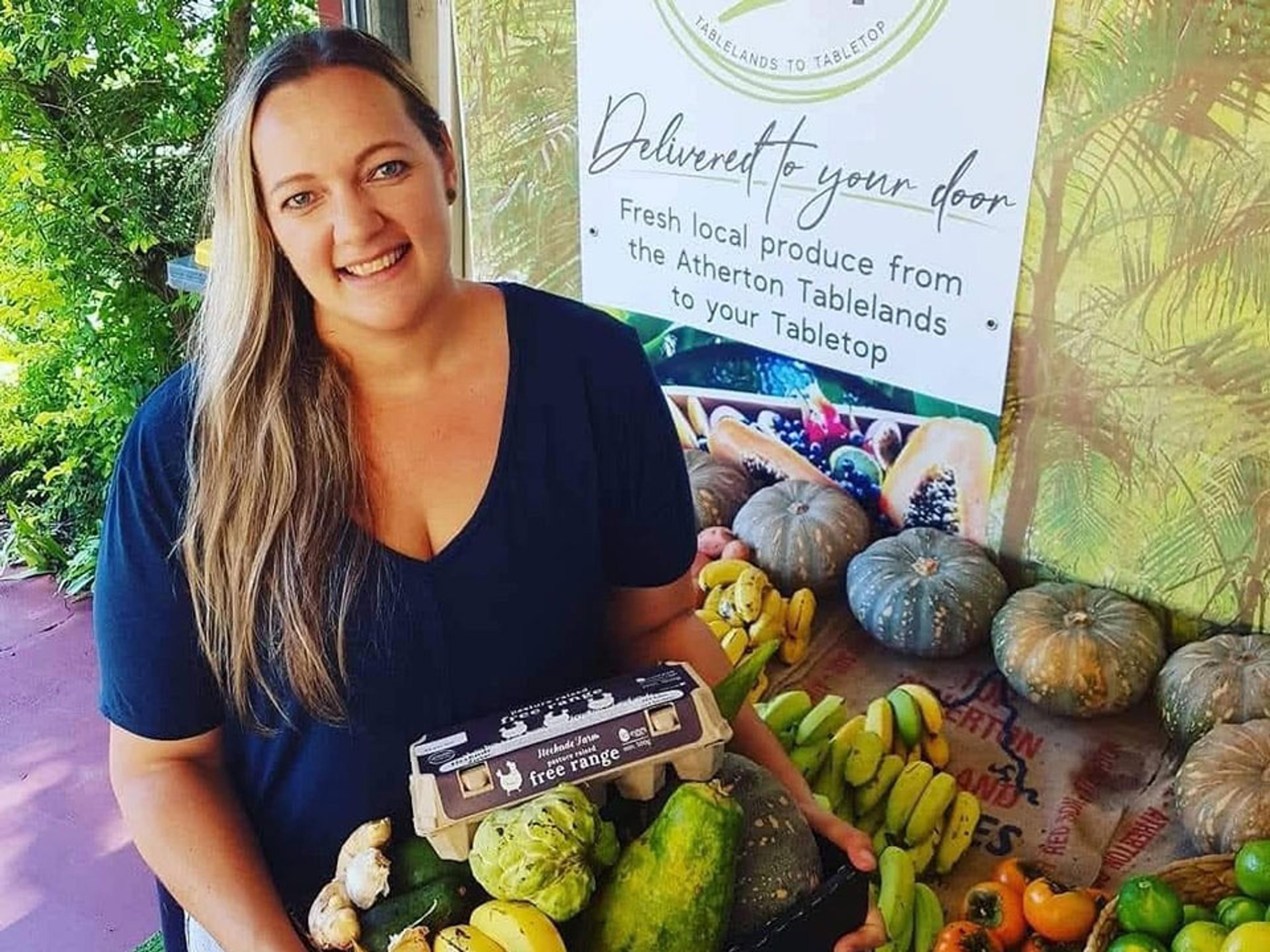 A smiling woman holding a box of fresh local produce.