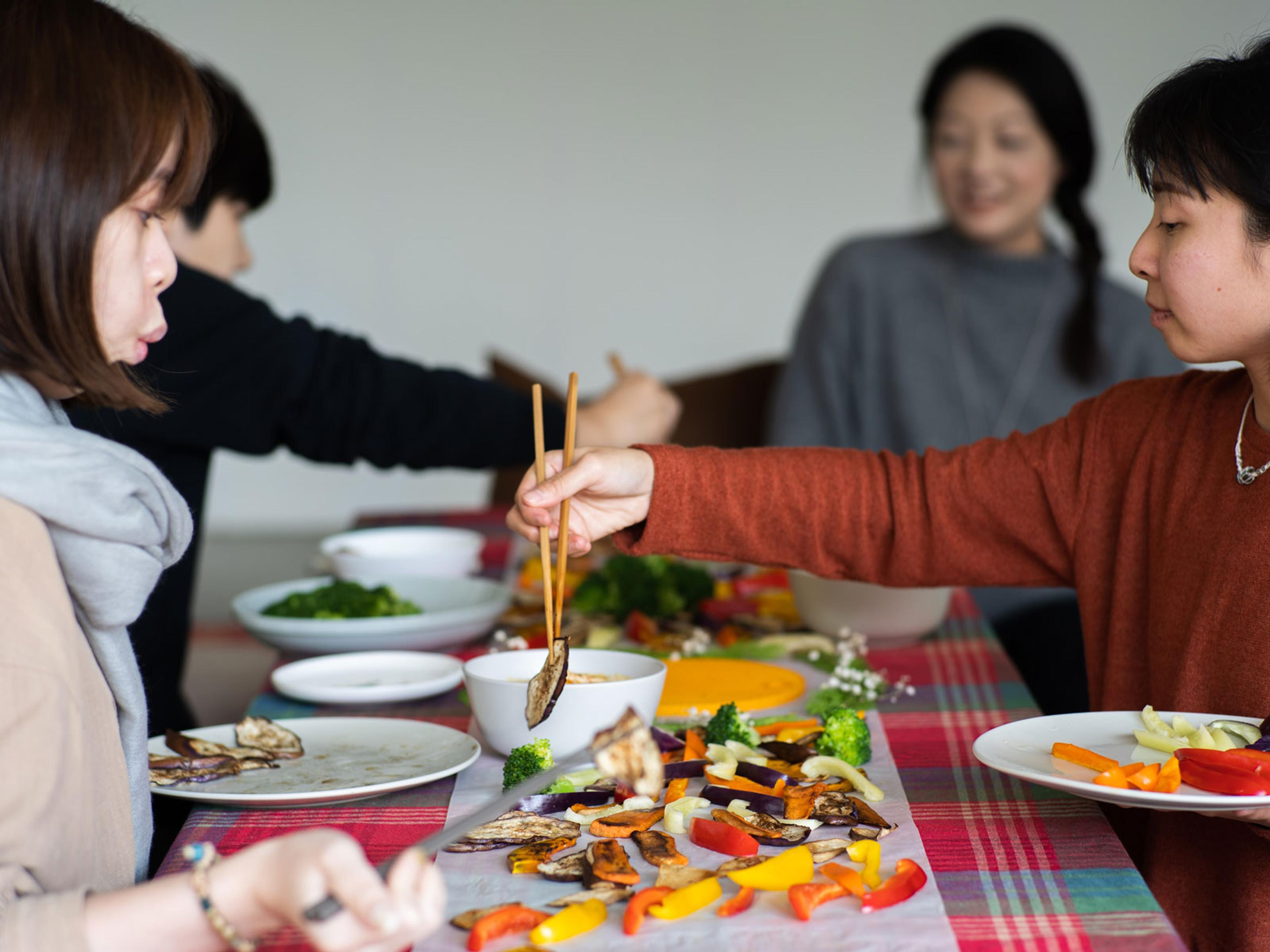 People sharing a meal. One person is picking up food from the middle of the table with chopsticks.